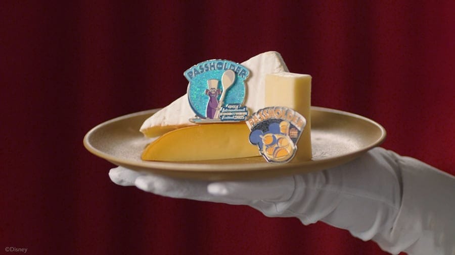 A gloved hand holds a plate with three cheeses and two colorful pins at the EPCOT International Food & Wine Festival.