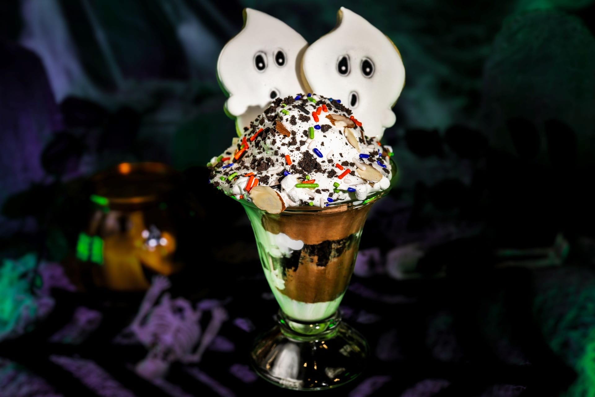 A Halloween sundae topped with whipped cream, sprinkles, and two ghost-shaped cookies.