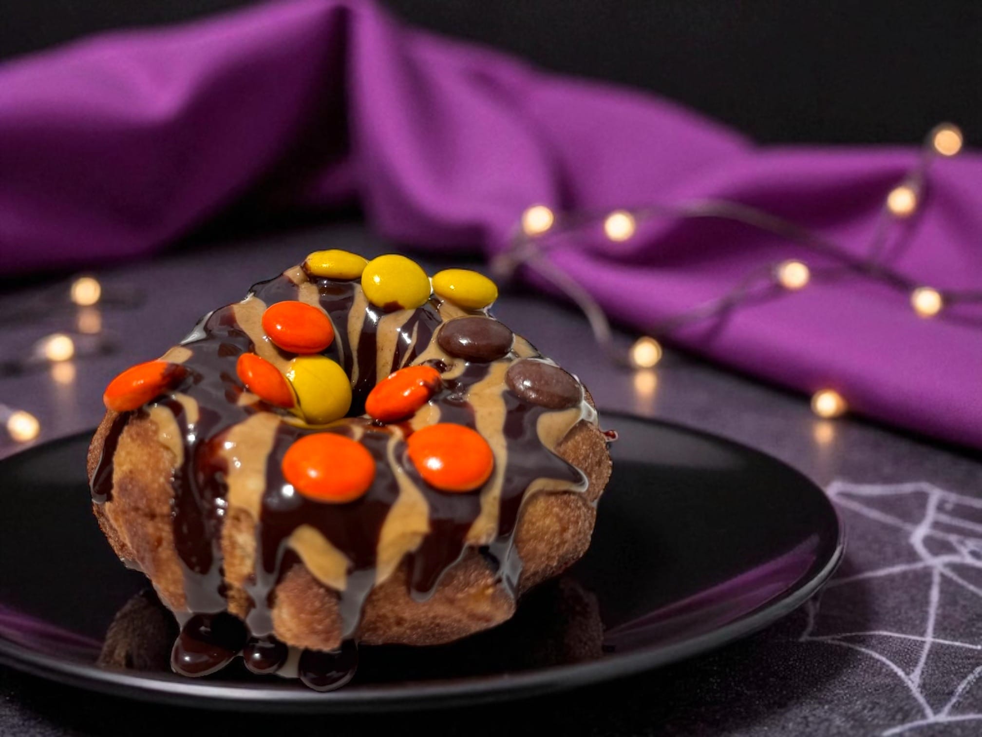 A 2025 Halloween Treats donut with chocolate, peanut butter, and candy sits on a black plate at Walt Disney World.