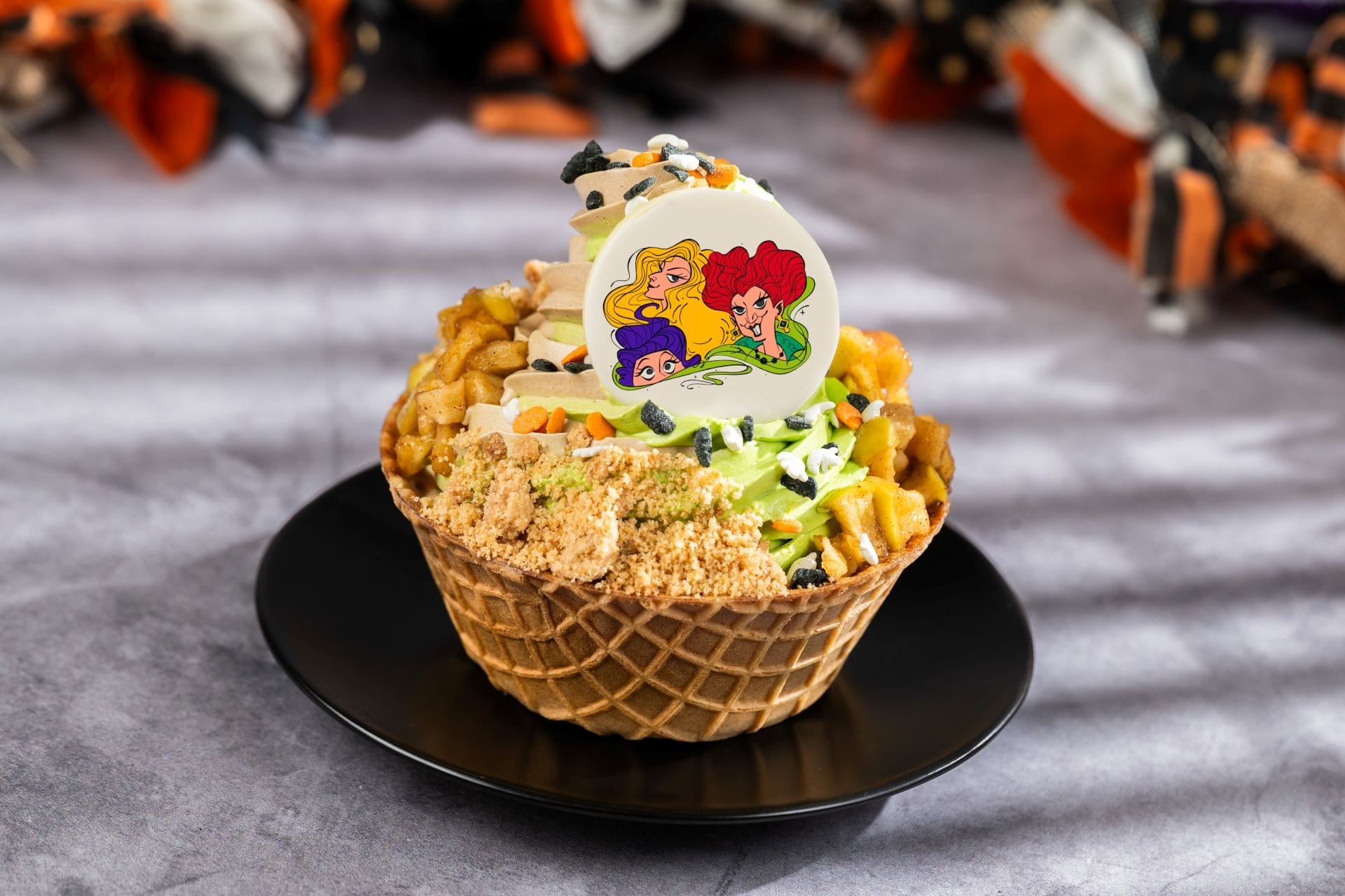 A waffle bowl with ice cream, festive toppings, and a white candy featuring three cartoon witches' faces—perfect for Halloween!