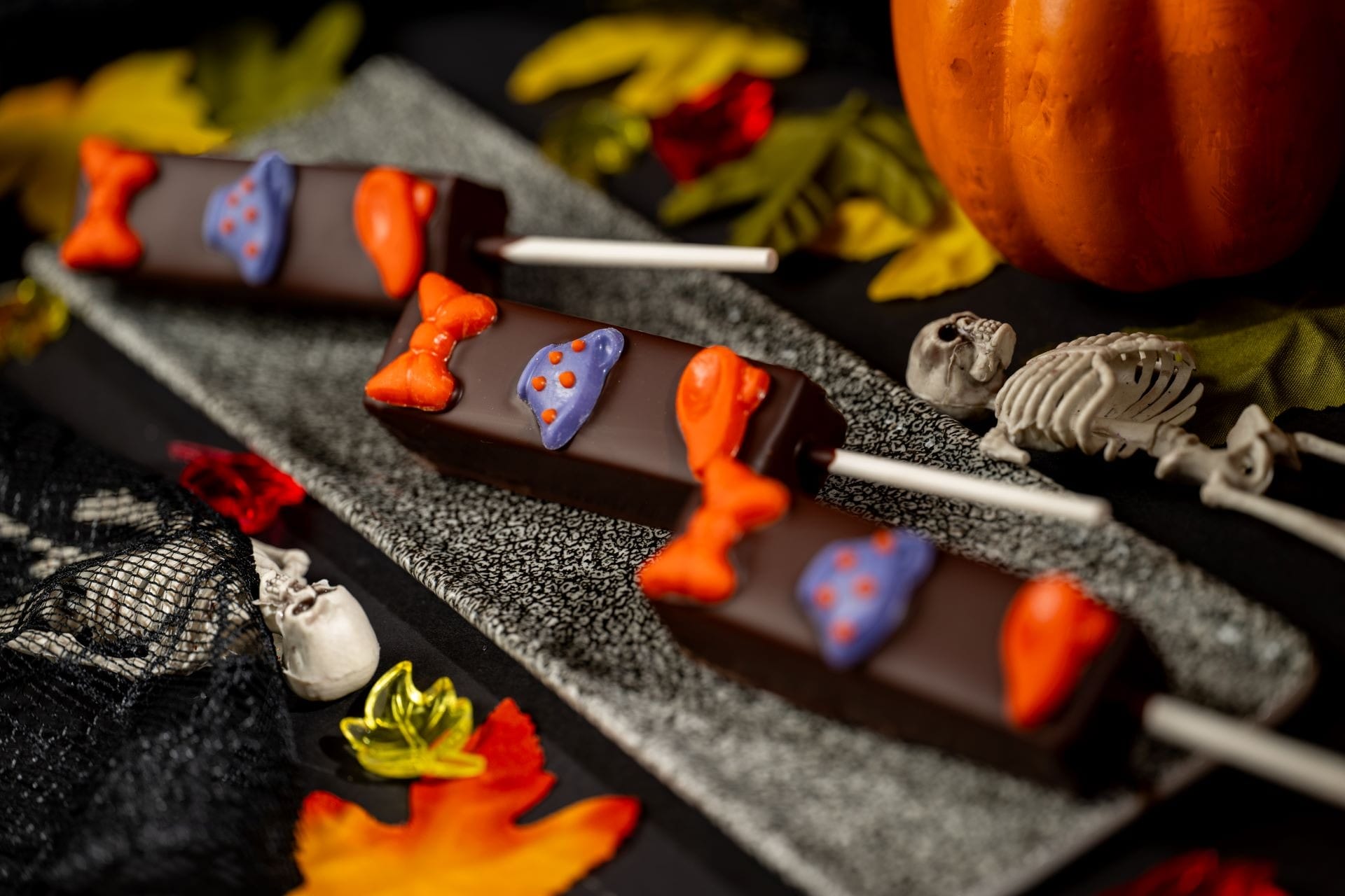 Three Halloween Treats: chocolate pops with festive icing, leaves, skulls, and a pumpkin—perfect for 2025 celebrations!