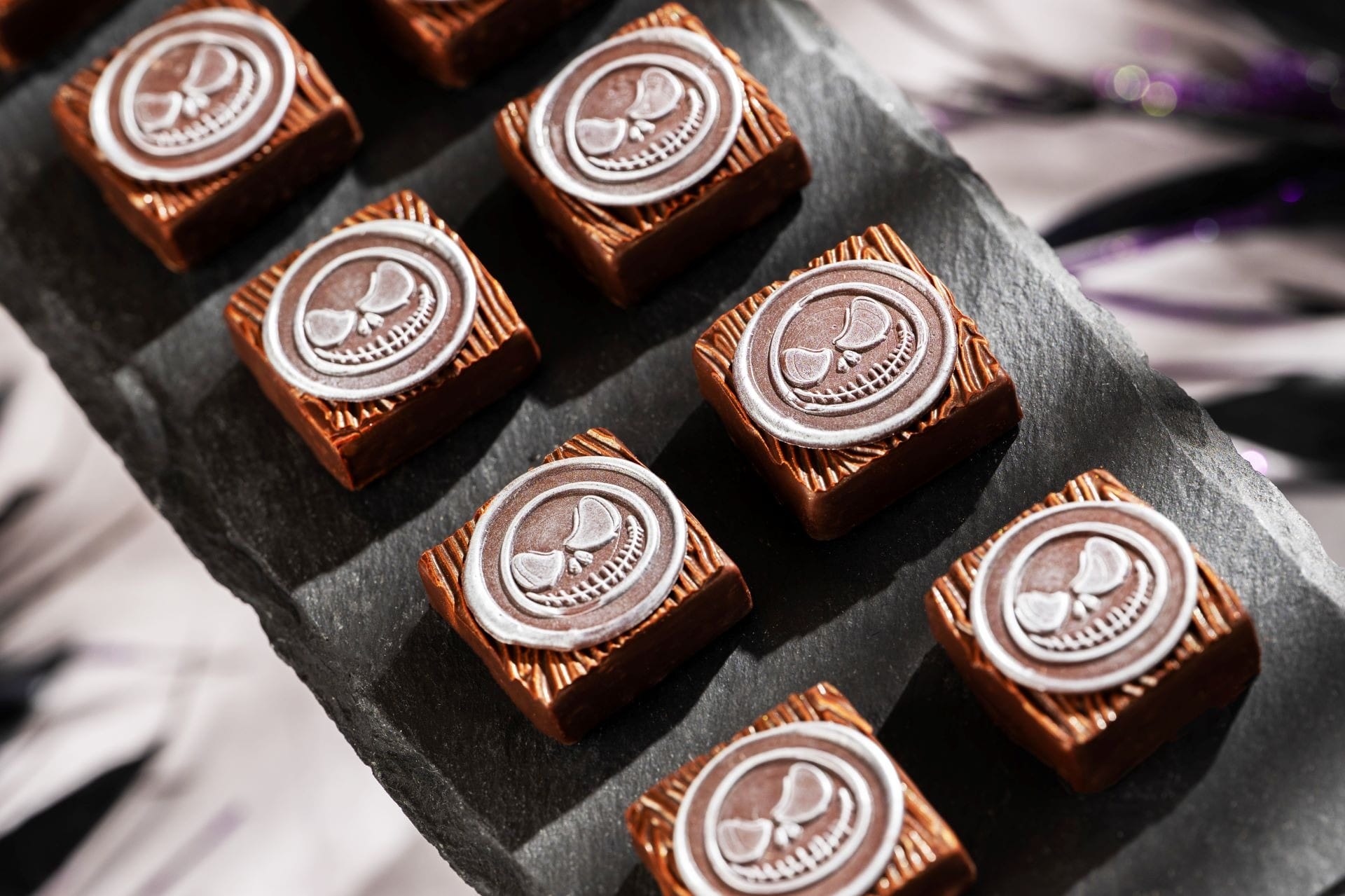 Nine square chocolates with silver skulls, inspired by 2025 Halloween treats, rest on a black slate serving tray.