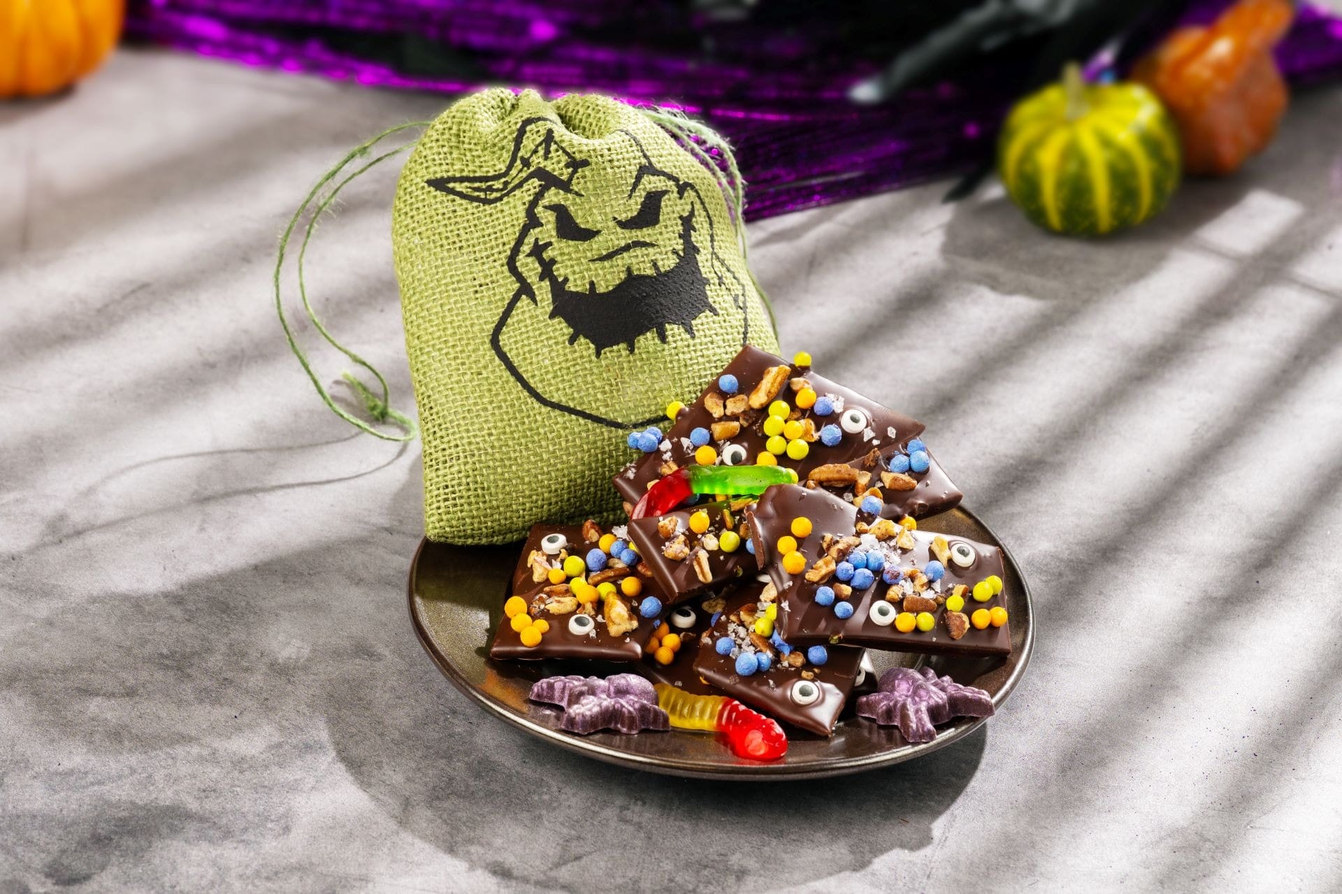 A plate of Halloween Treats chocolate bark and a spooky green bag, with pumpkins—perfect for 2025 at Walt Disney World.