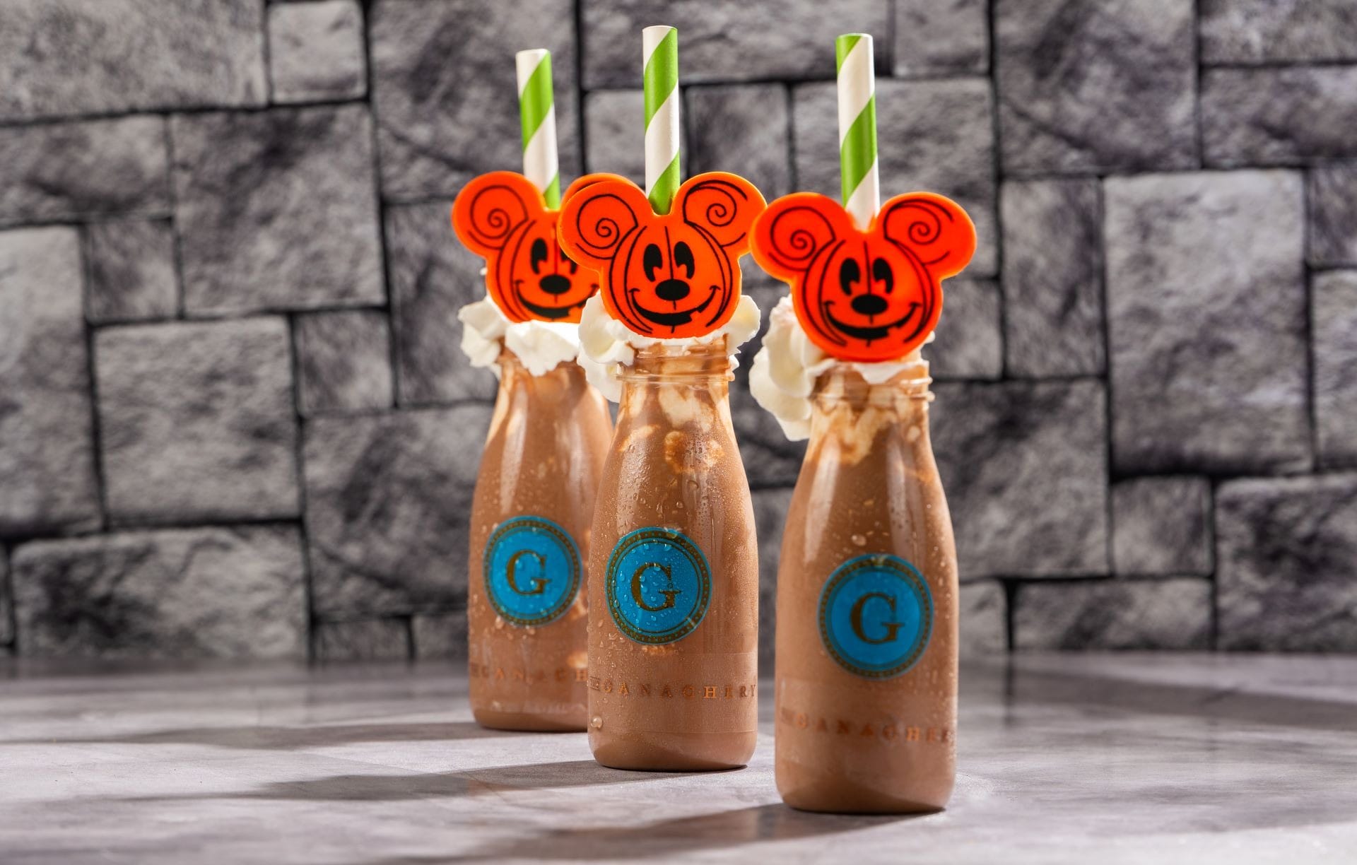 Three chocolate milkshakes in glass bottles, topped with whipped cream and 2025 Halloween Treats at Walt Disney World.