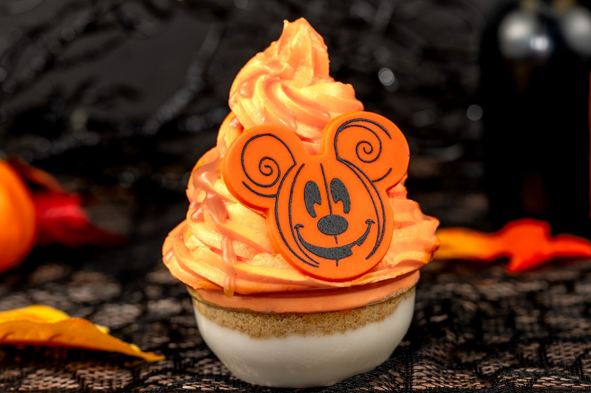 Halloween cupcake with orange frosting, a cartoon topper, and fall leaves—perfect for 2025 Halloween treats.