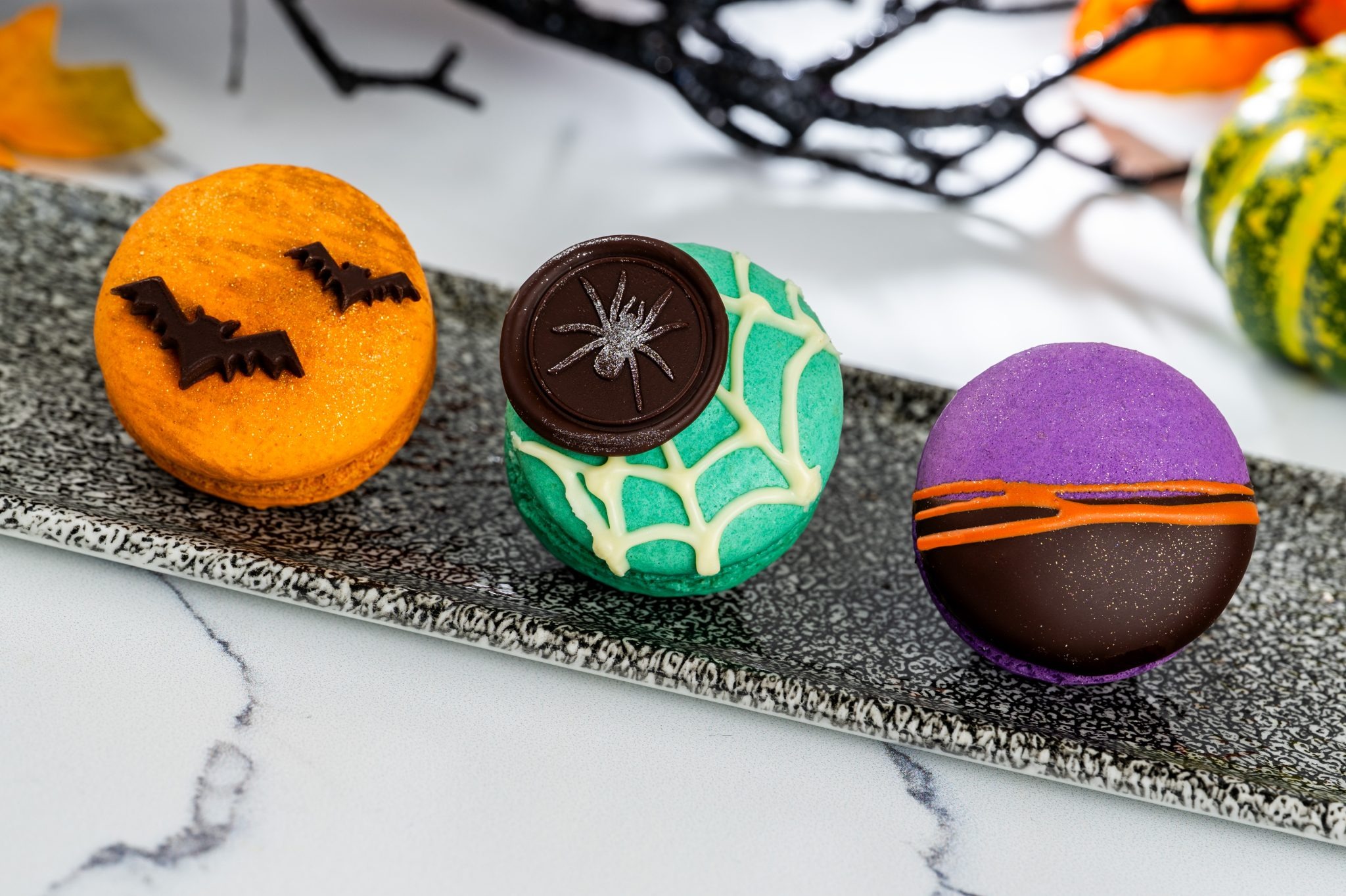 Three colorful 2025 Halloween Treats macarons, including a bat and spiderweb, on a tray at Walt Disney World.