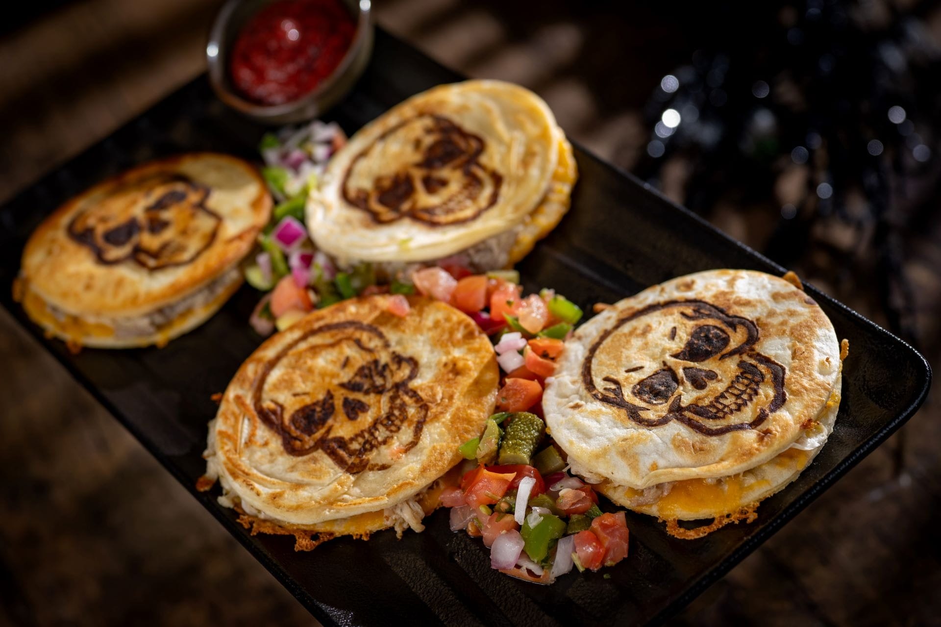 Four quesadillas with skull designs, part of the 2025 Halloween Treats at Walt Disney World, served with salsa and salad.
