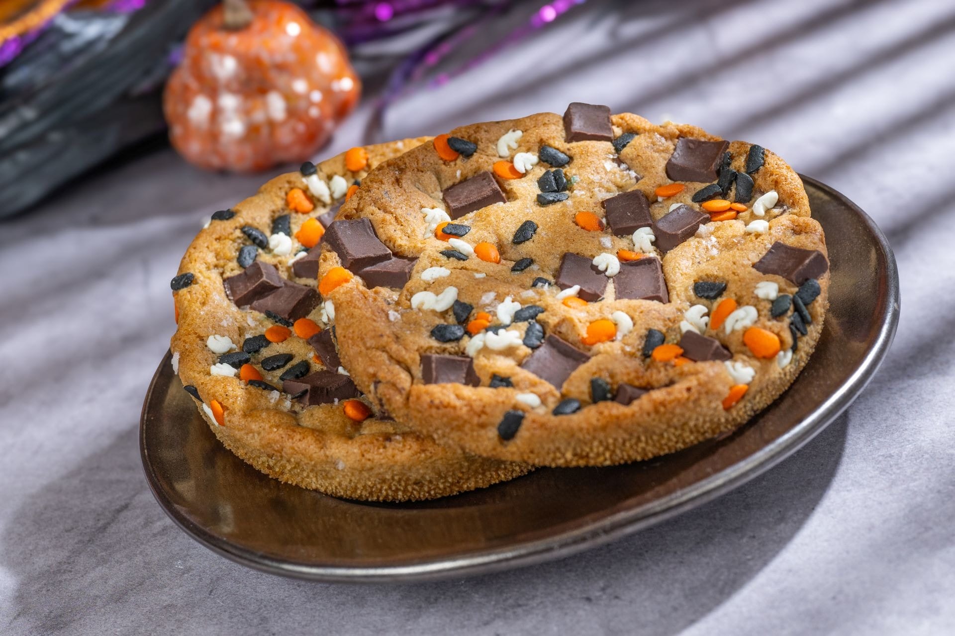 Two large cookies with chocolate chunks and orange, black, and white sprinkles on a brown plate.