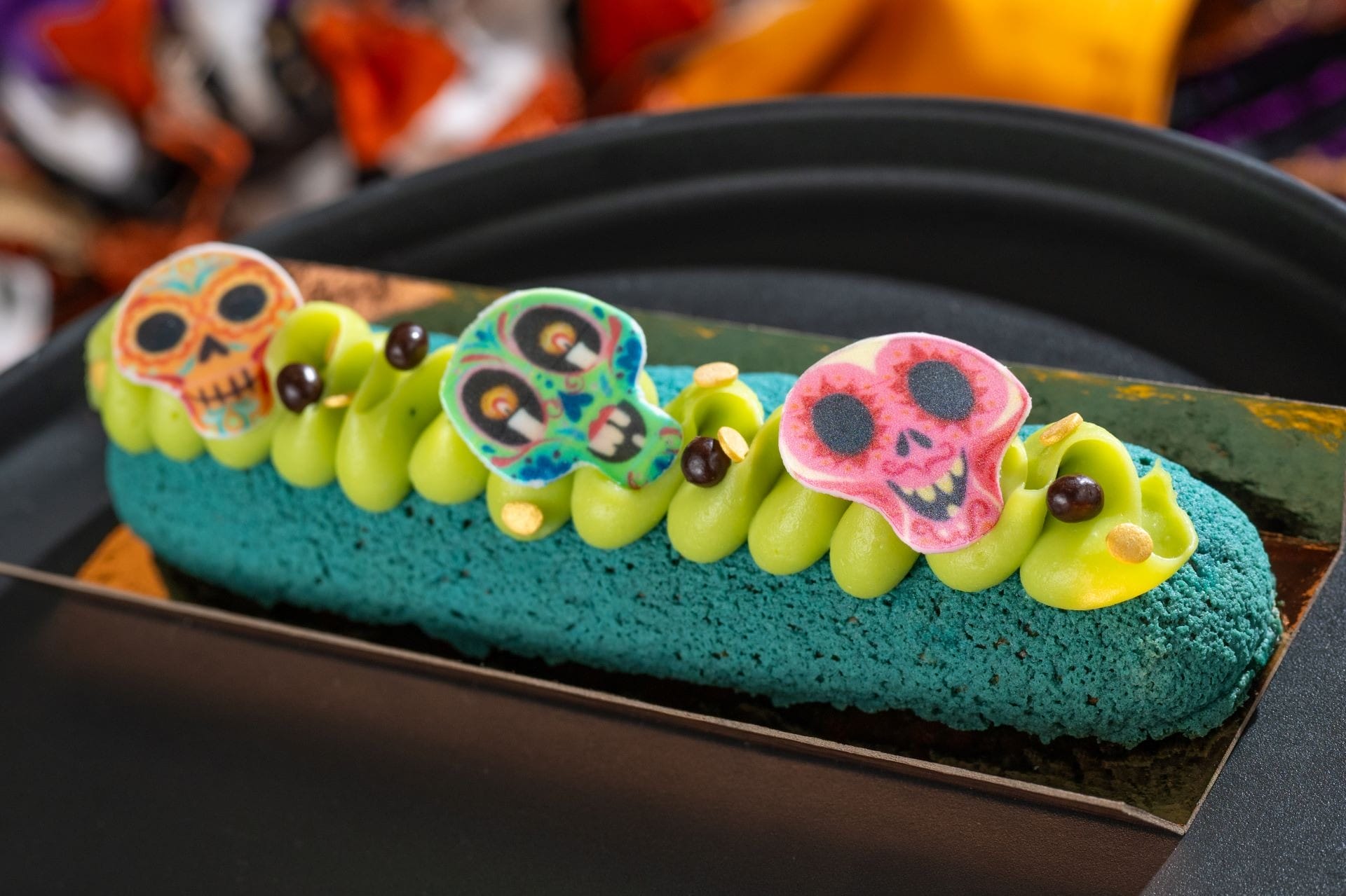 A colorful pastry decorated with green frosting and three Day of the Dead sugar skull toppers.