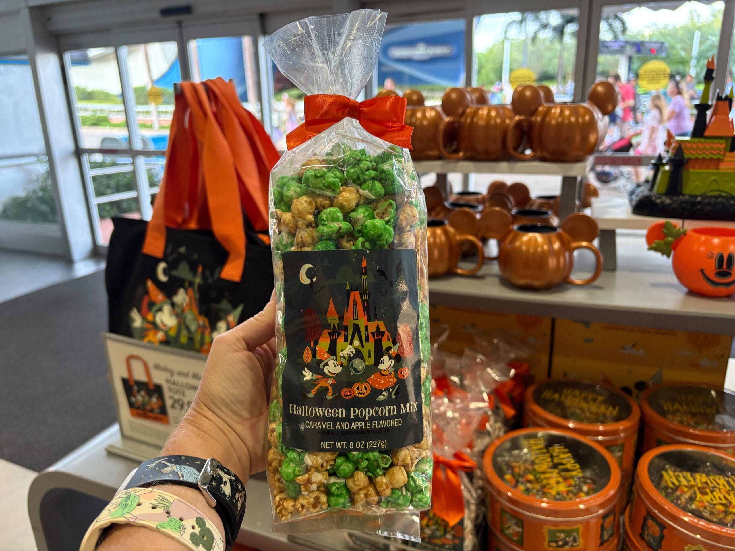 A hand holds Disney Halloween Merch caramel apple popcorn in a store with festive 2025 Walt Disney World decorations.