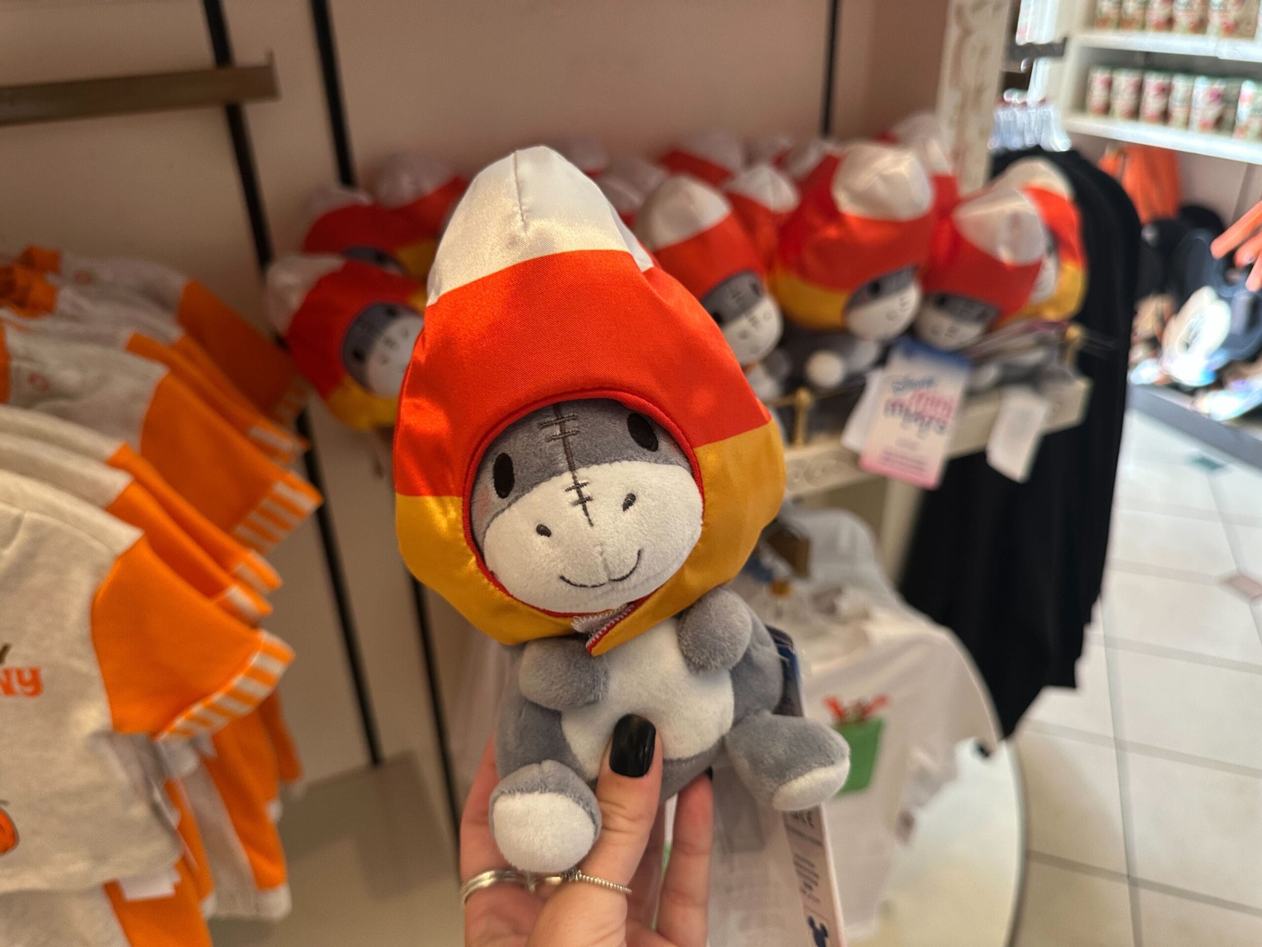 A hand holds a plush donkey in a candy corn costume—part of Disney Halloween Merch 2025 at Walt Disney World.