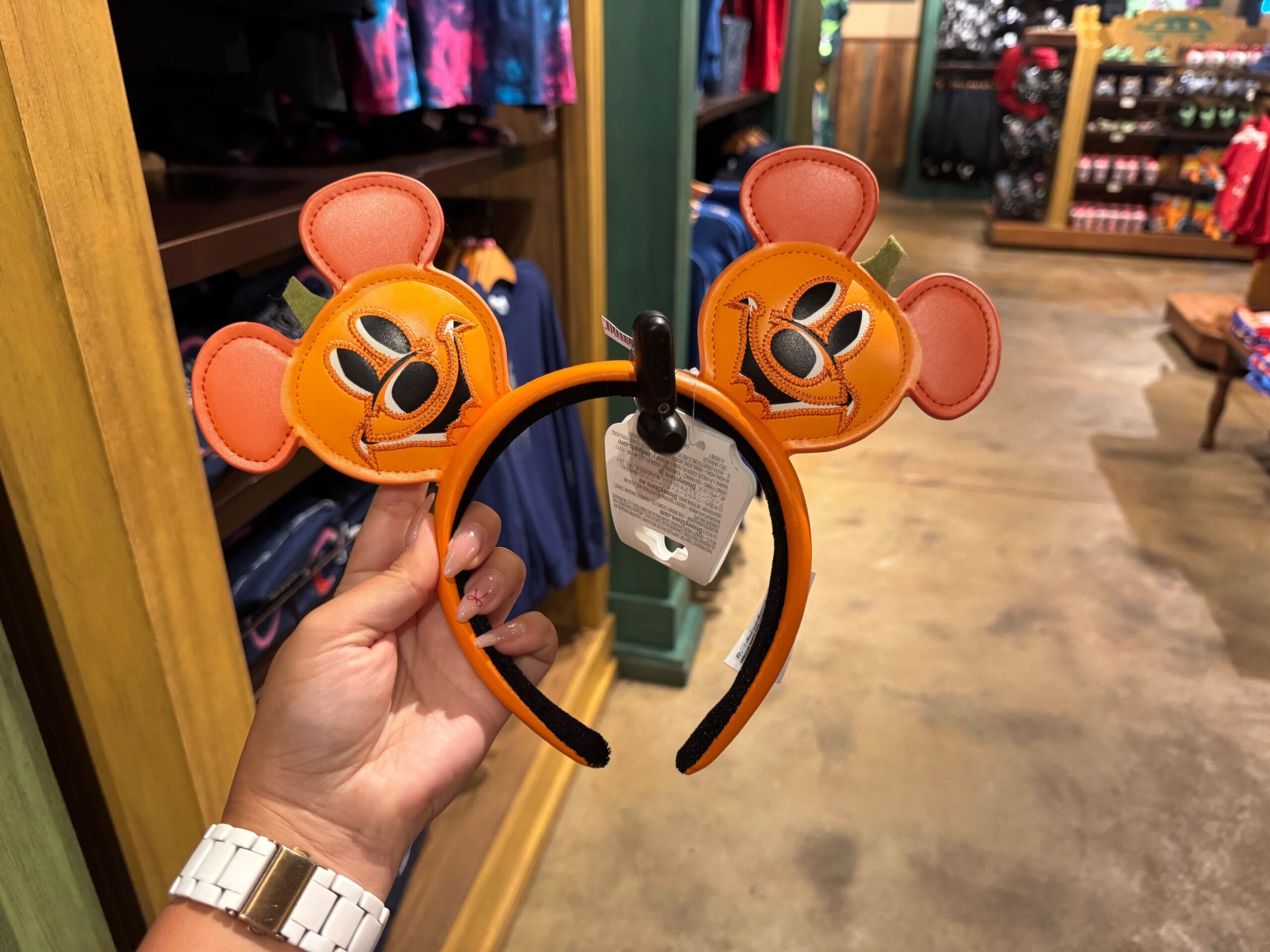 Hand holding orange Mickey Mouse ear headband with pumpkin face design—fun Halloween merchandise at Walt Disney World.
