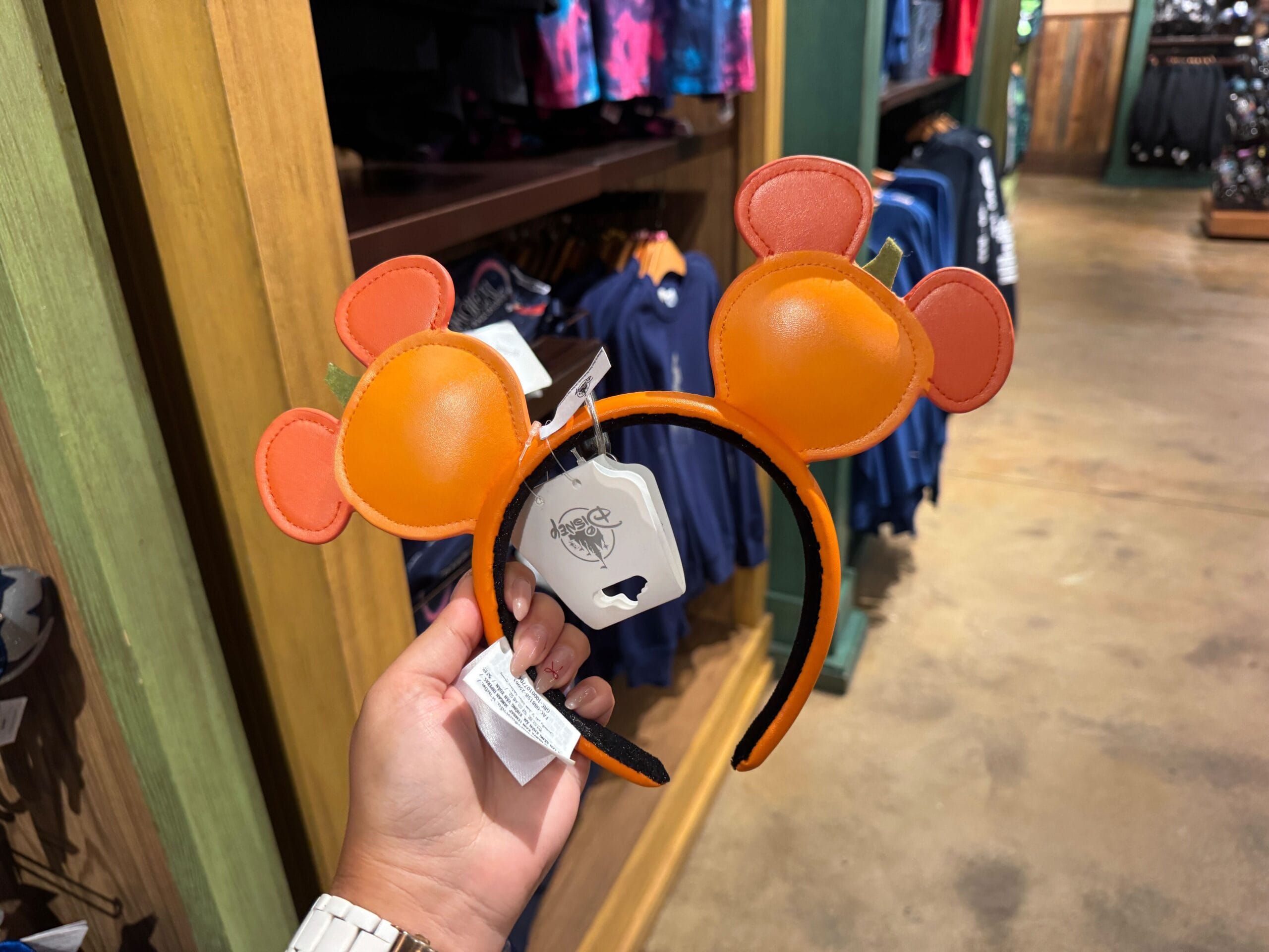 Hand holding an orange Mickey Mouse ear headband, part of the Halloween merchandise at Walt Disney World store.