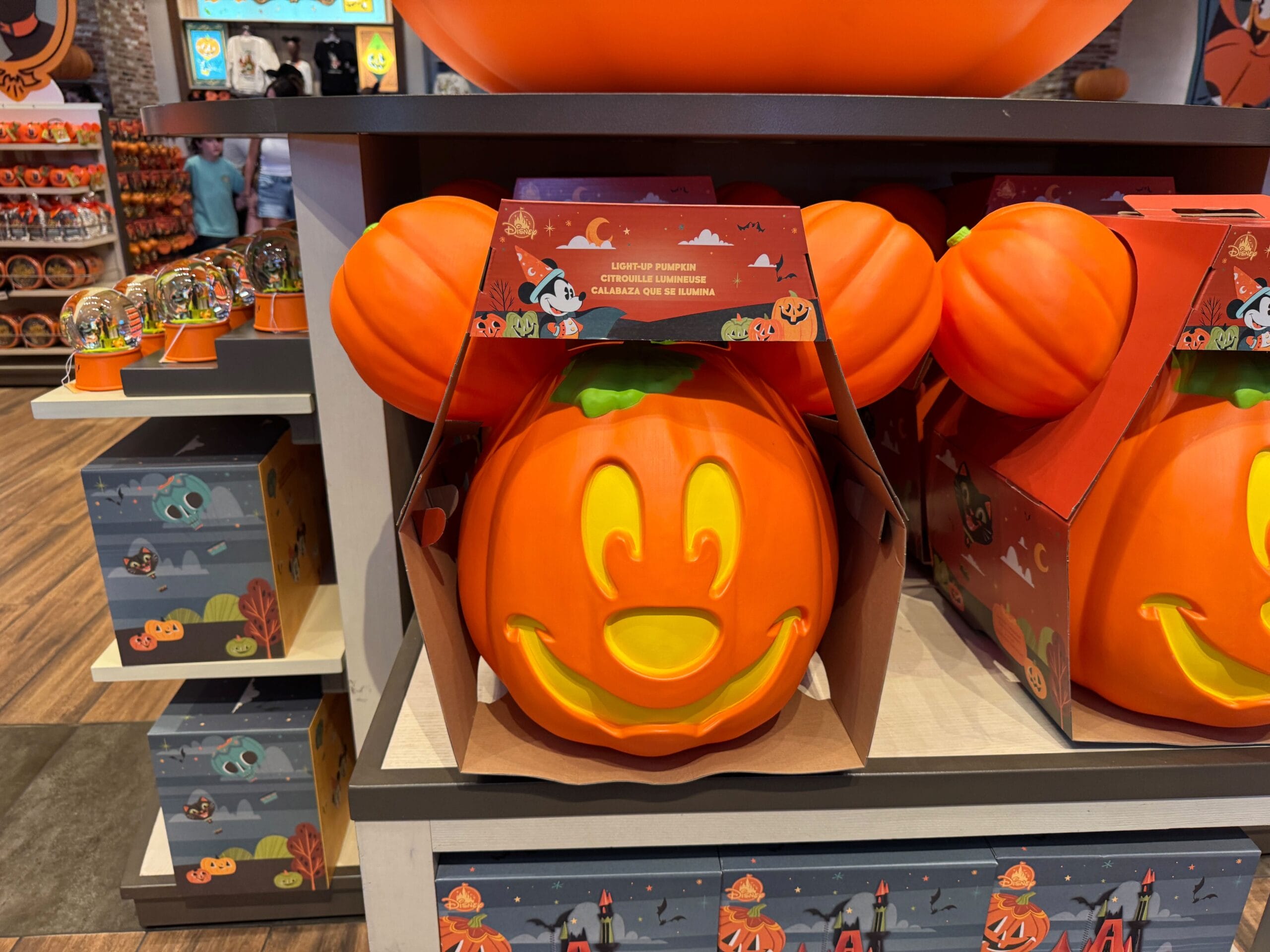 A Mickey Mouse pumpkin bucket with a smiling face sits among Halloween merchandise on a store shelf.