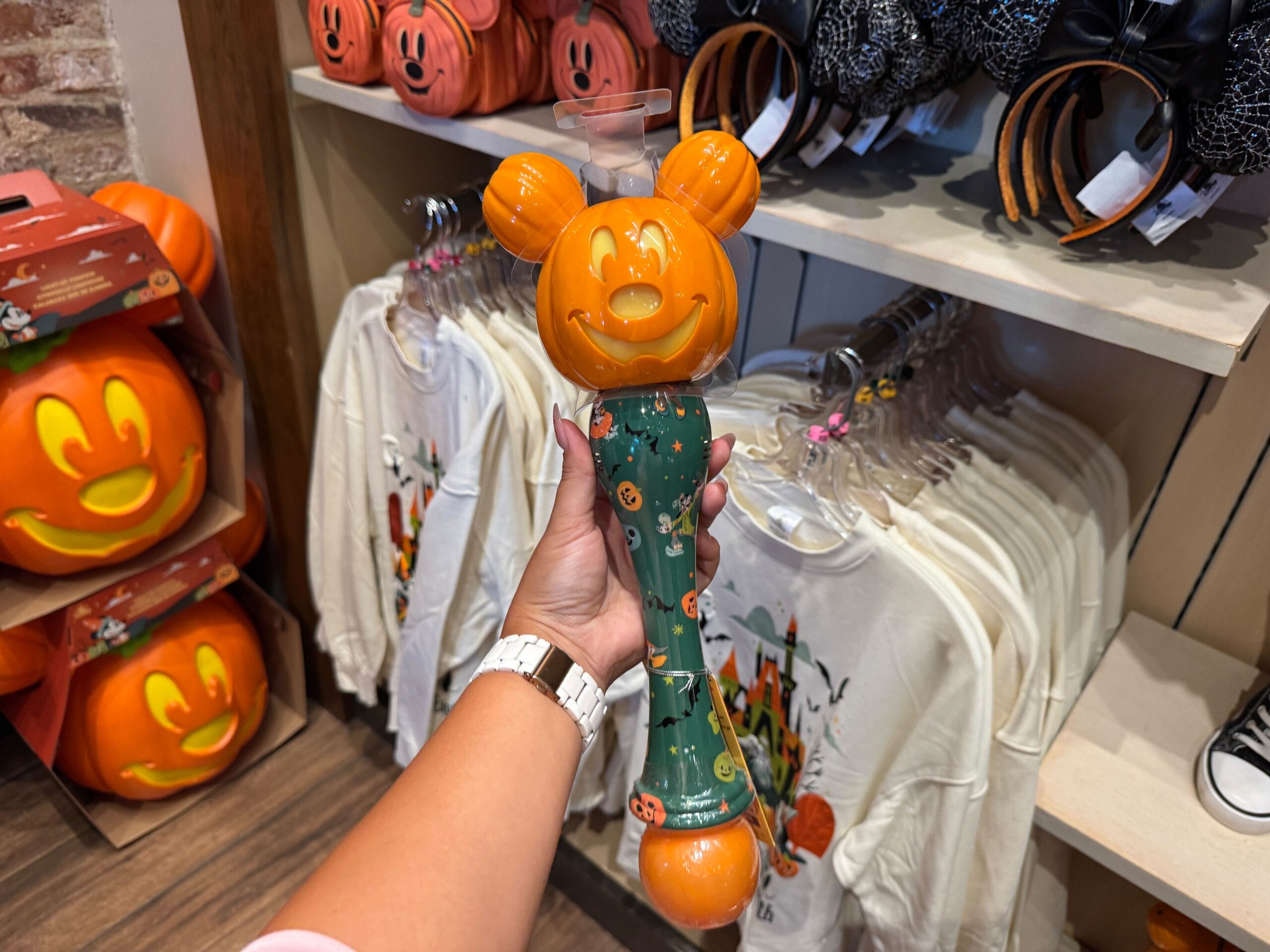 A hand holds a 2025 Halloween merchandise Mickey Mouse pumpkin popcorn bucket in a Walt Disney World store.
