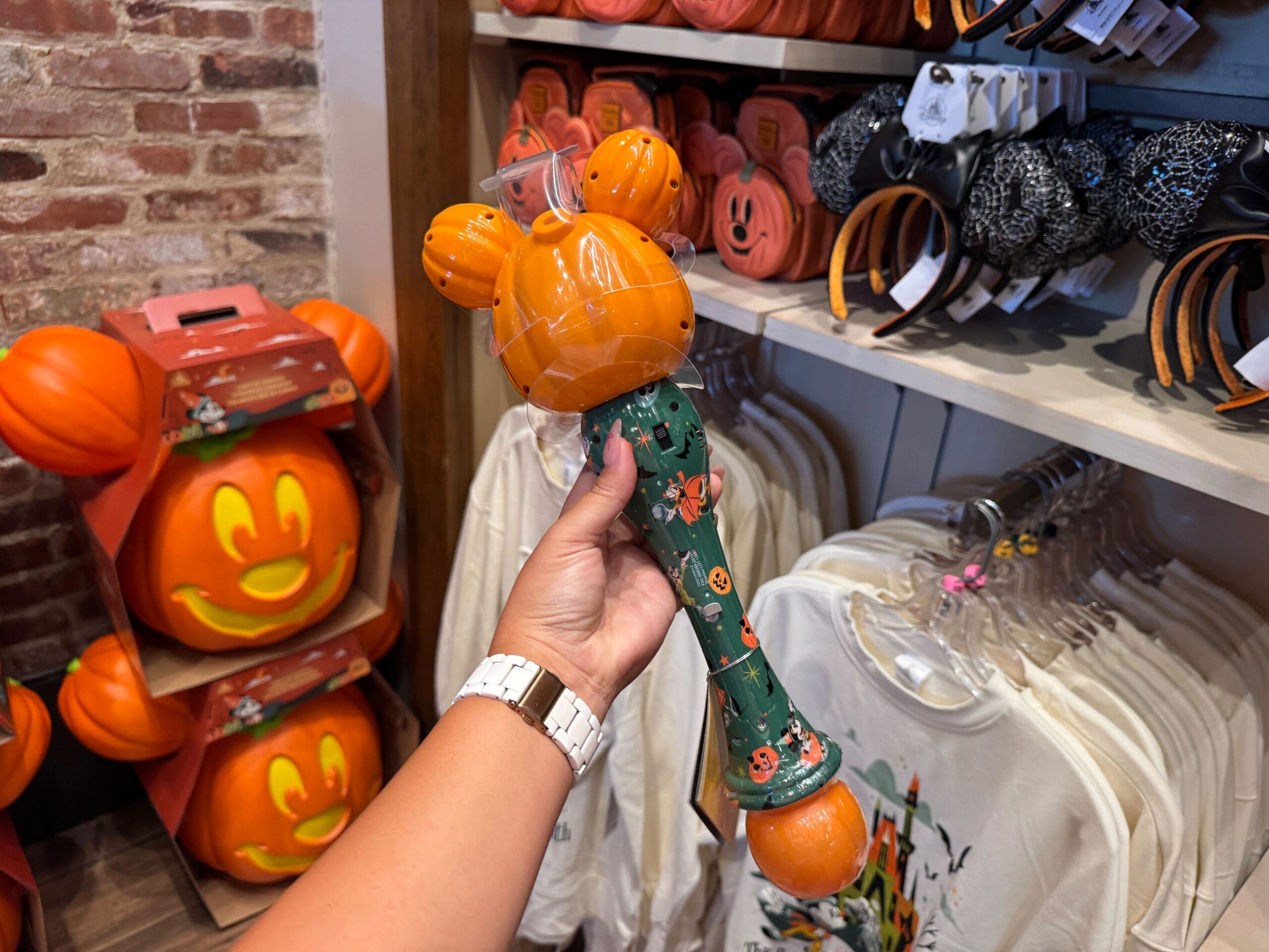 A person holds a Mickey Mouse pumpkin light-up wand among 2025 Halloween merchandise at Walt Disney World.