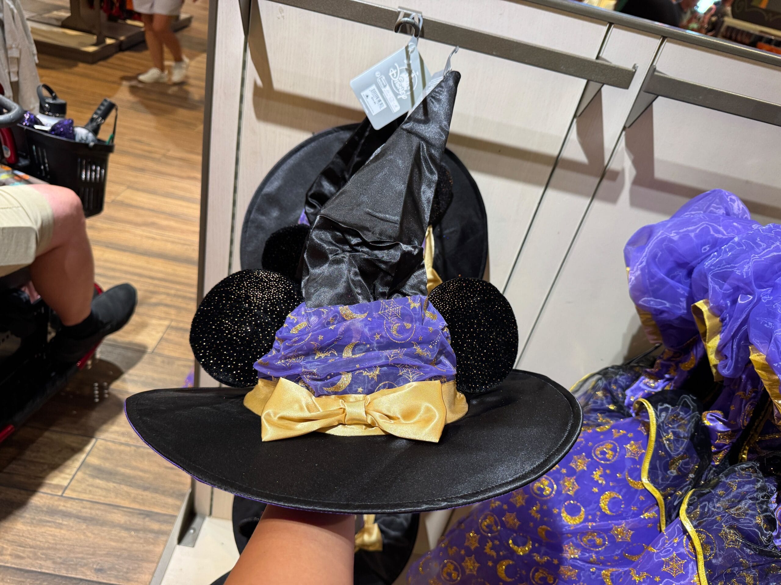 A hand holds a Minnie Mouse witch hat from Walt Disney World Halloween merchandise with black ears and gold bow.