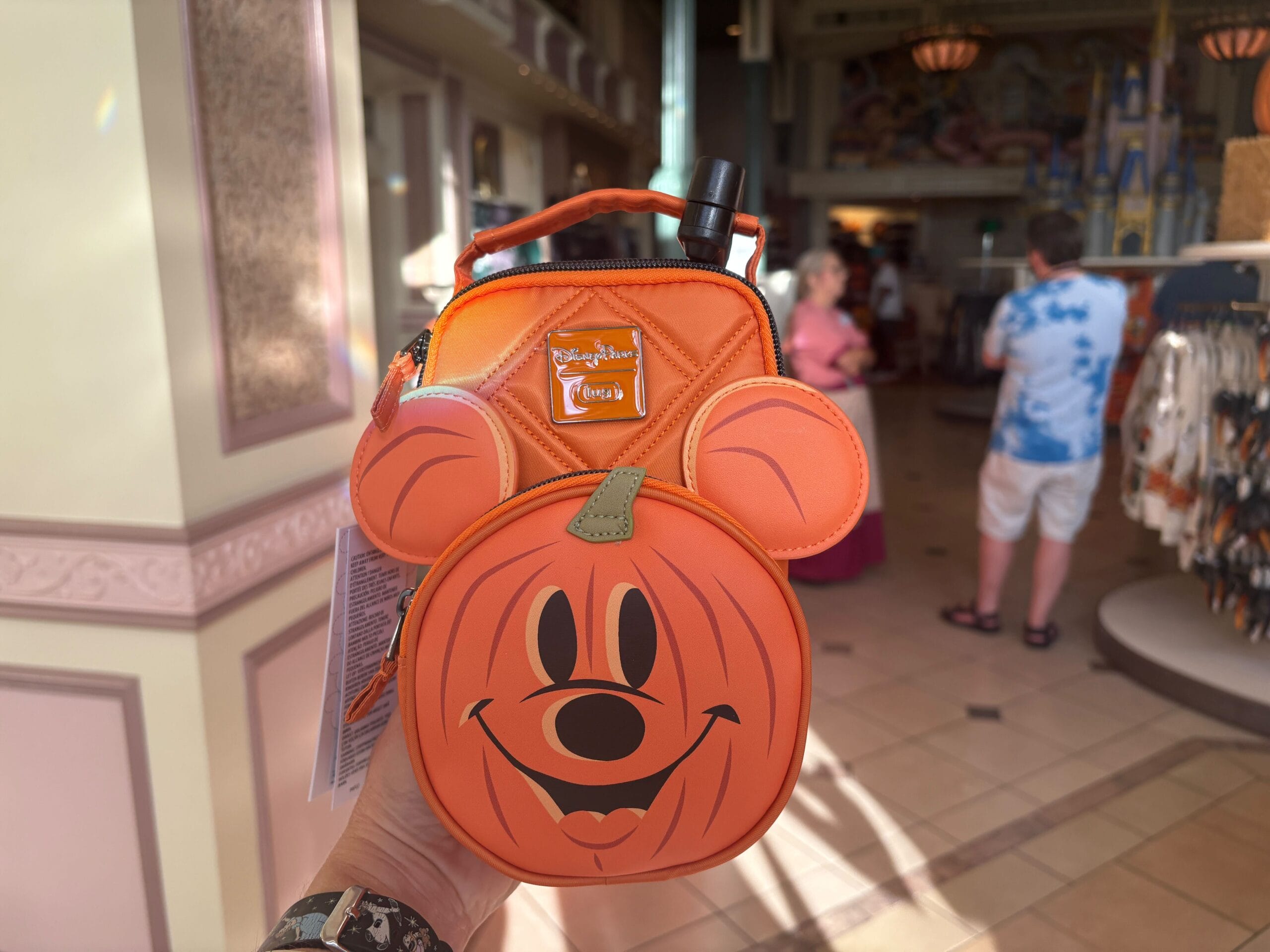 A hand holds an orange Mickey Mouse pumpkin-themed bag, showcasing Halloween merchandise at Walt Disney World.
