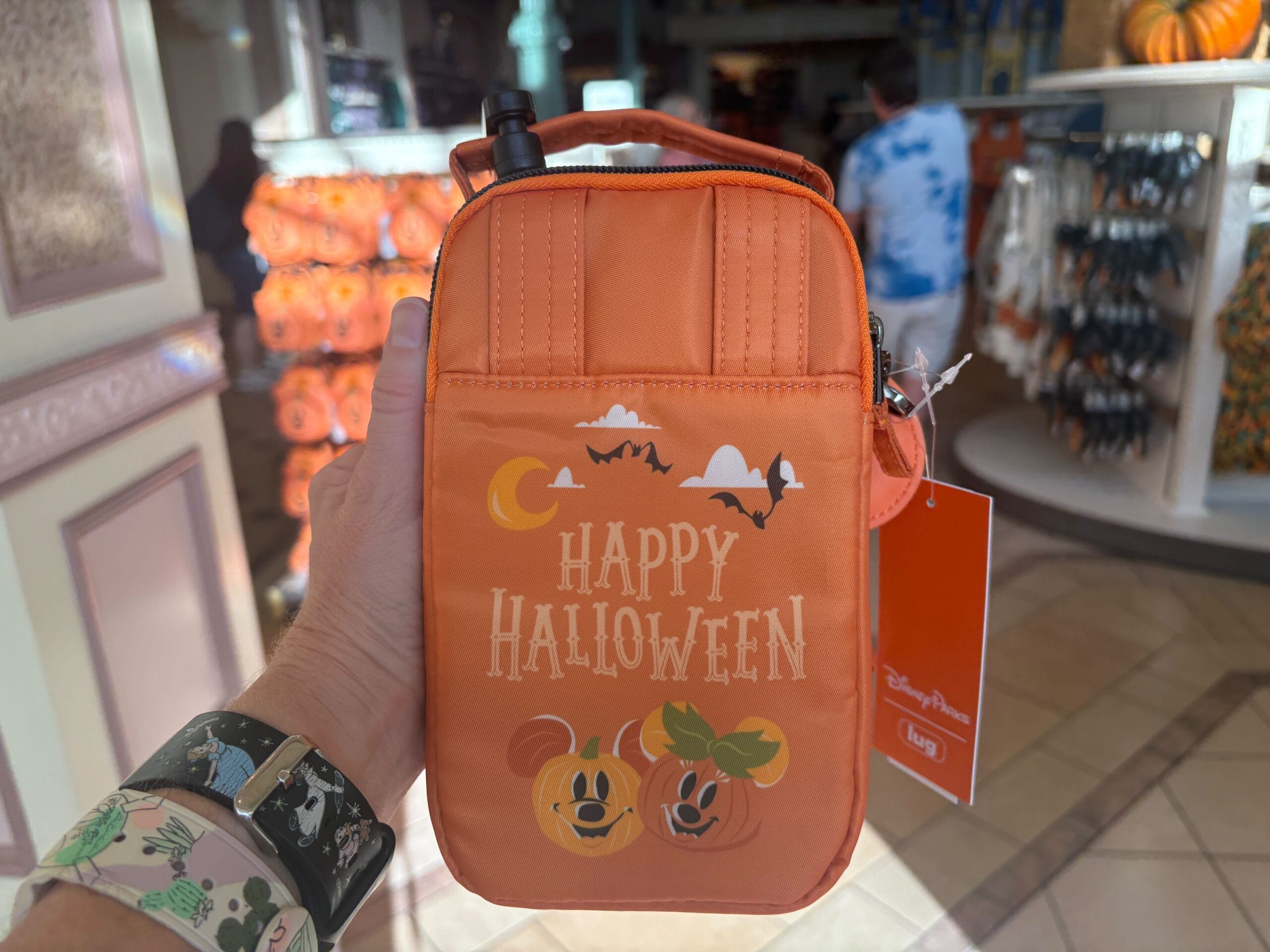 Hand holding an orange Disney Halloween Merchandise bag with Mickey pumpkin designs at Walt Disney World store.