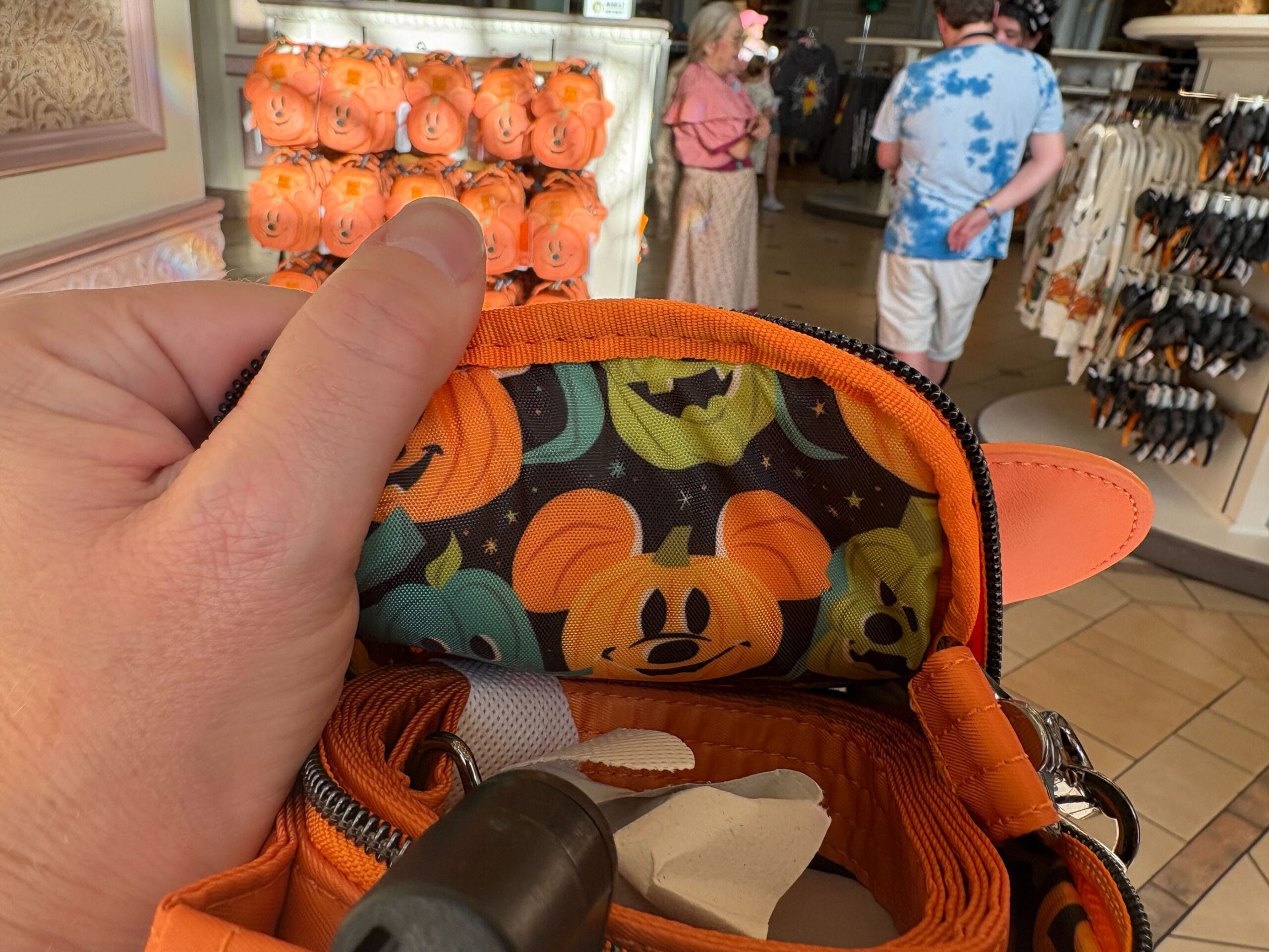 A hand holds open an orange Mickey pumpkin purse amid Halloween Merchandise at Walt Disney World.