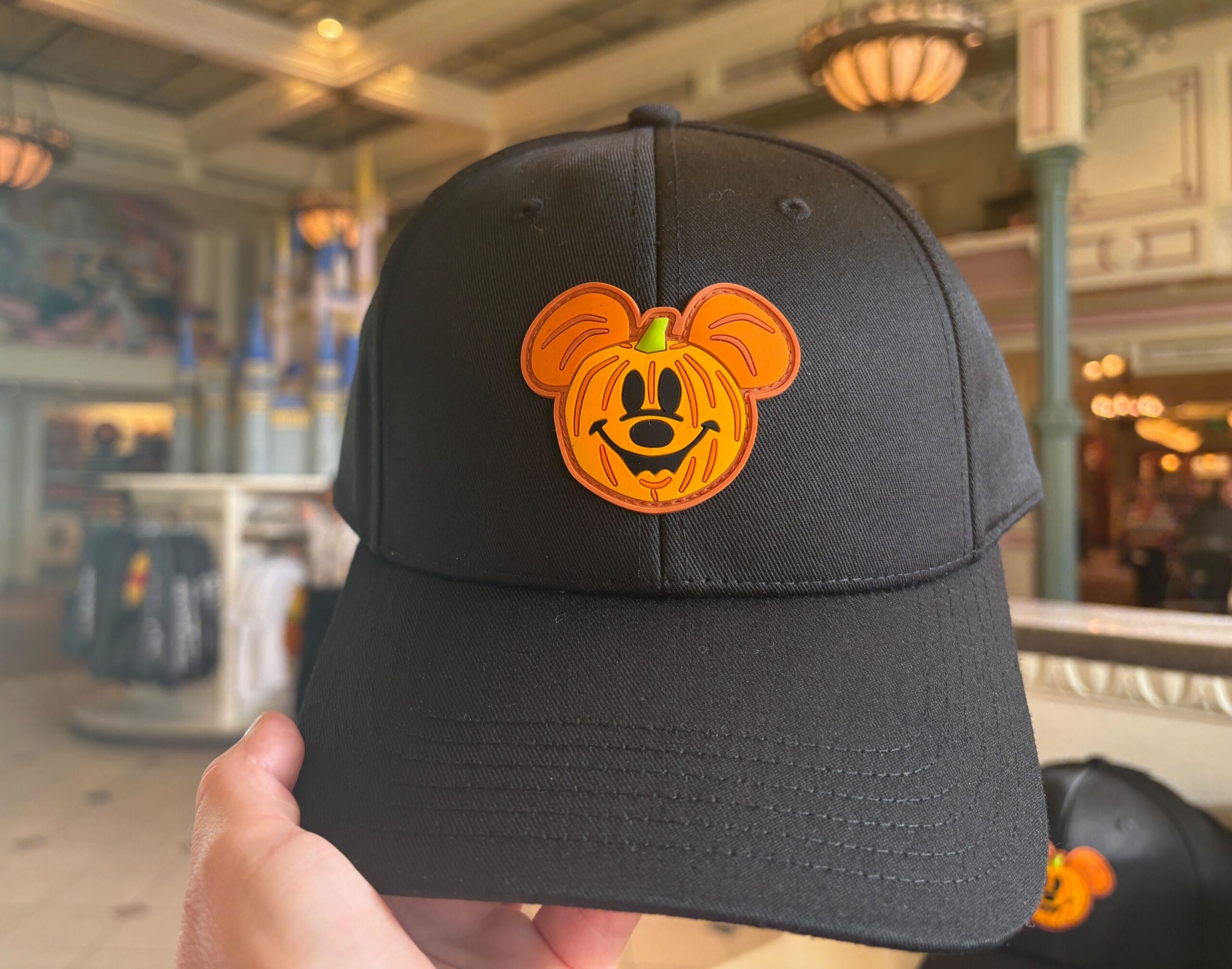 A black cap with an orange Mickey Mouse pumpkin logo, part of Halloween merchandise at Walt Disney World.