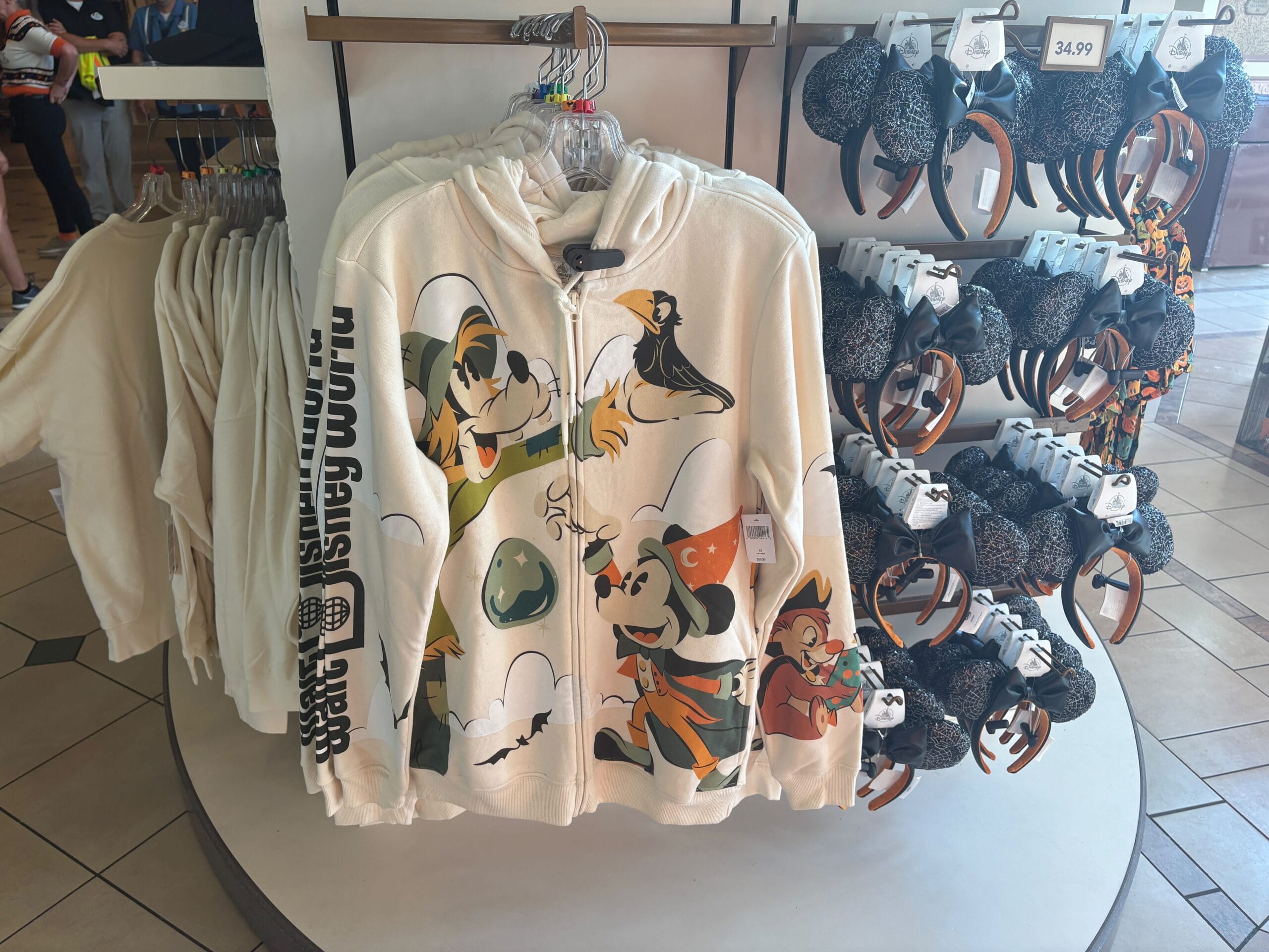 White hoodie with Walt Disney World Halloween merchandise displayed near black Minnie Mouse ear headbands.