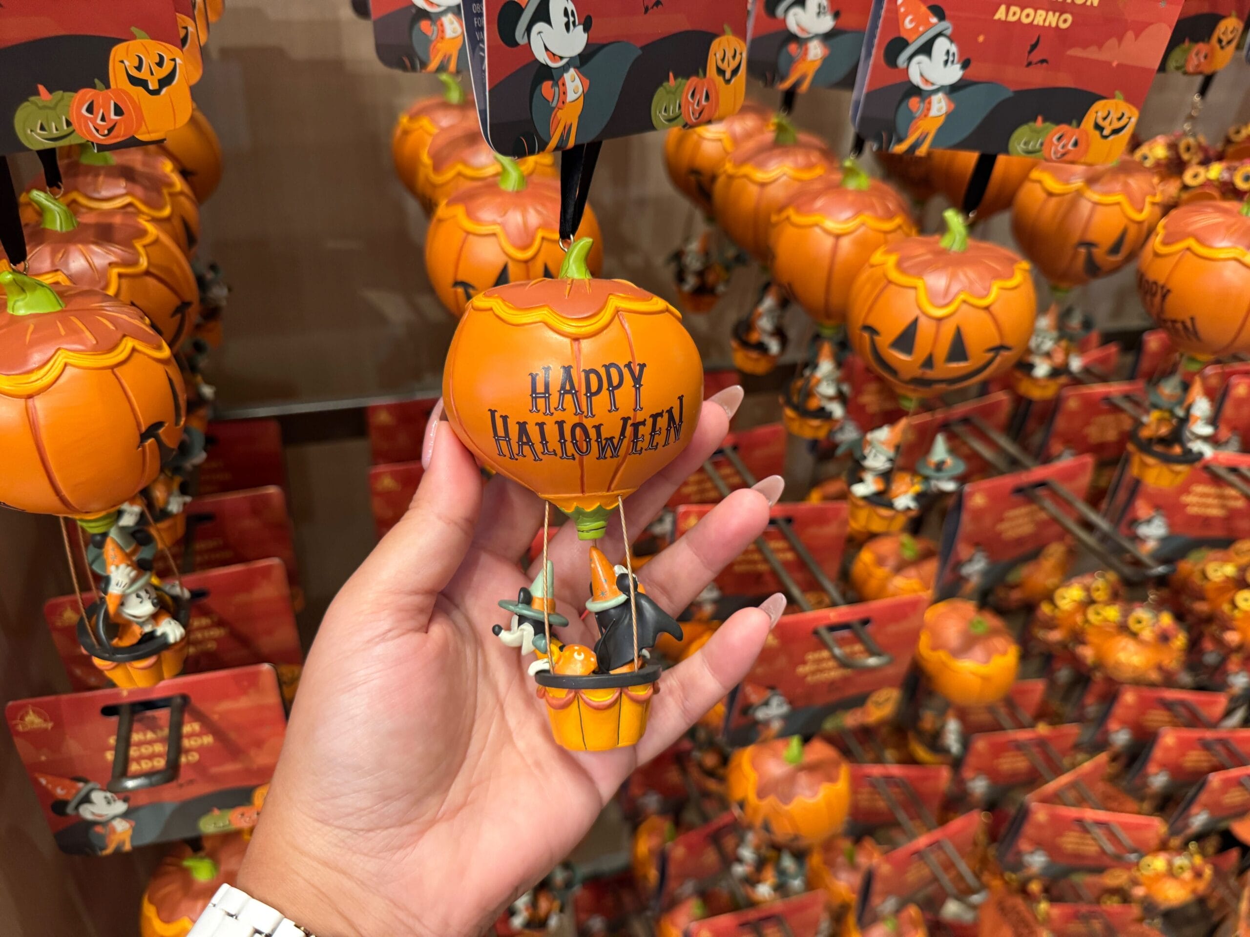Hand holding a pumpkin-shaped 2025 Halloween merchandise ornament at Walt Disney World, surrounded by similar ornaments.