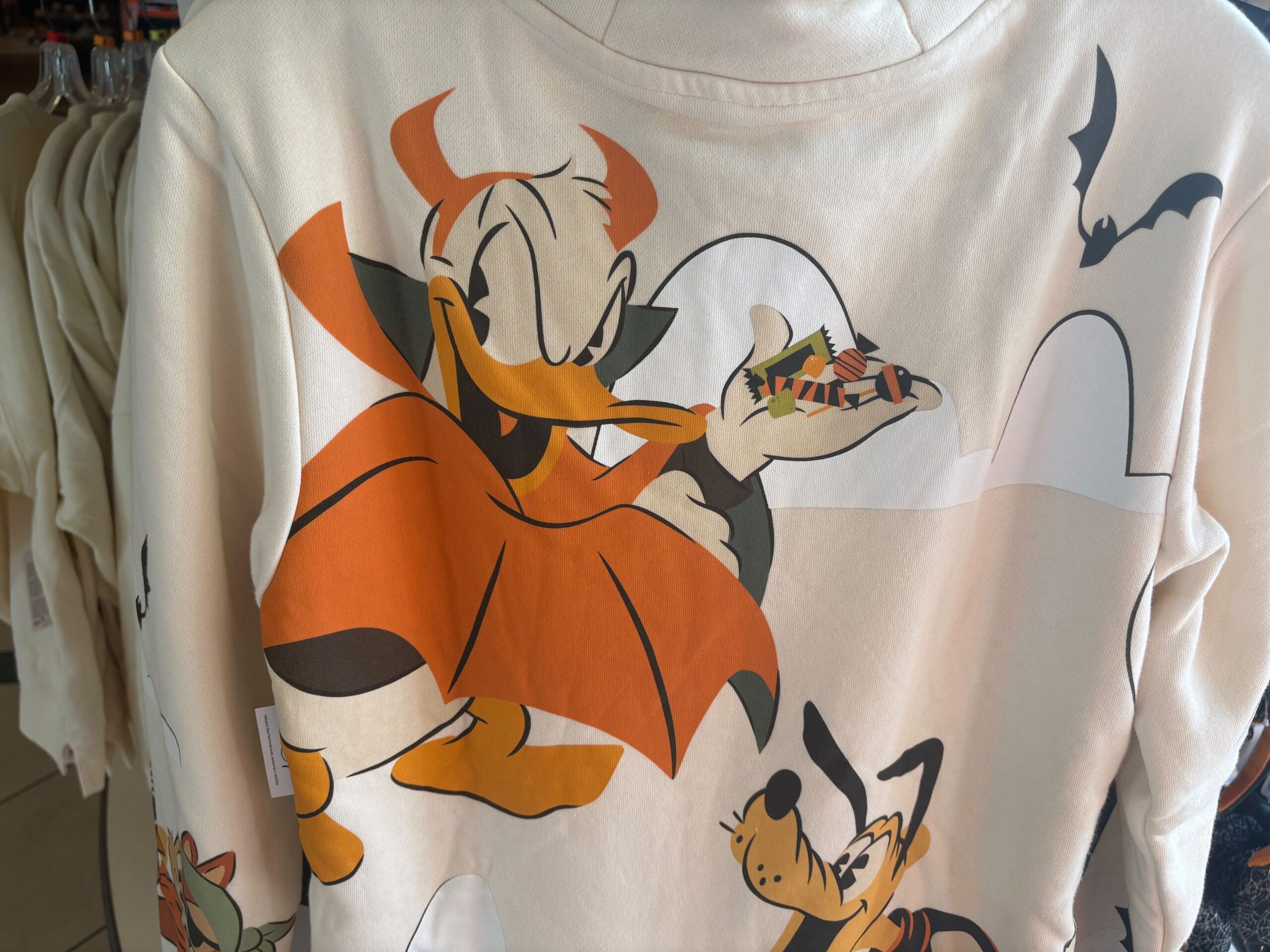 Cartoon duck in a vampire costume holds candy, with bats and dog on a white shirt—fun Halloween merchandise at Walt Disney World.