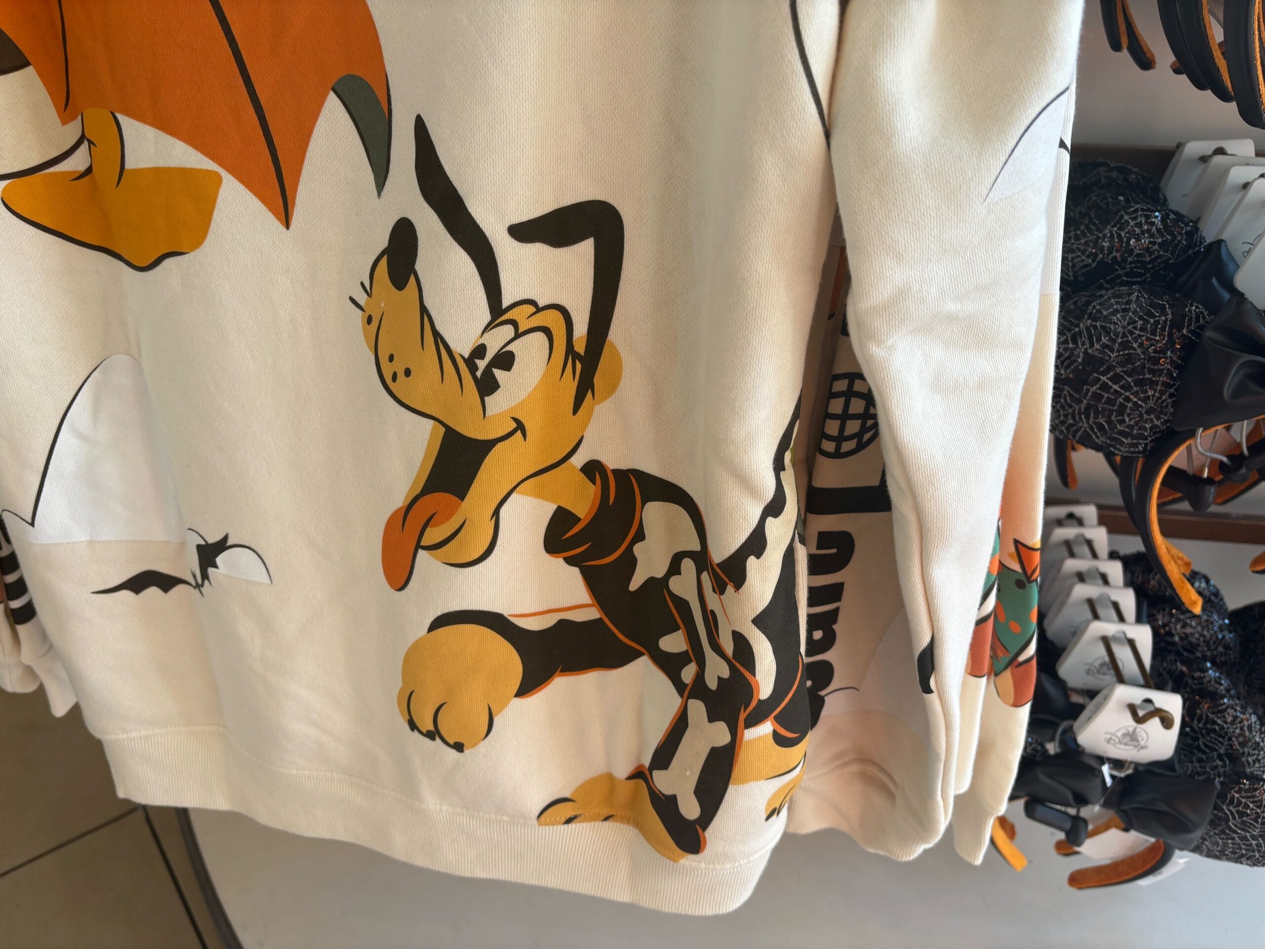White sweatshirt featuring Disney’s Pluto with a cartoon skeleton, perfect Halloween merchandise on a clothing rack.