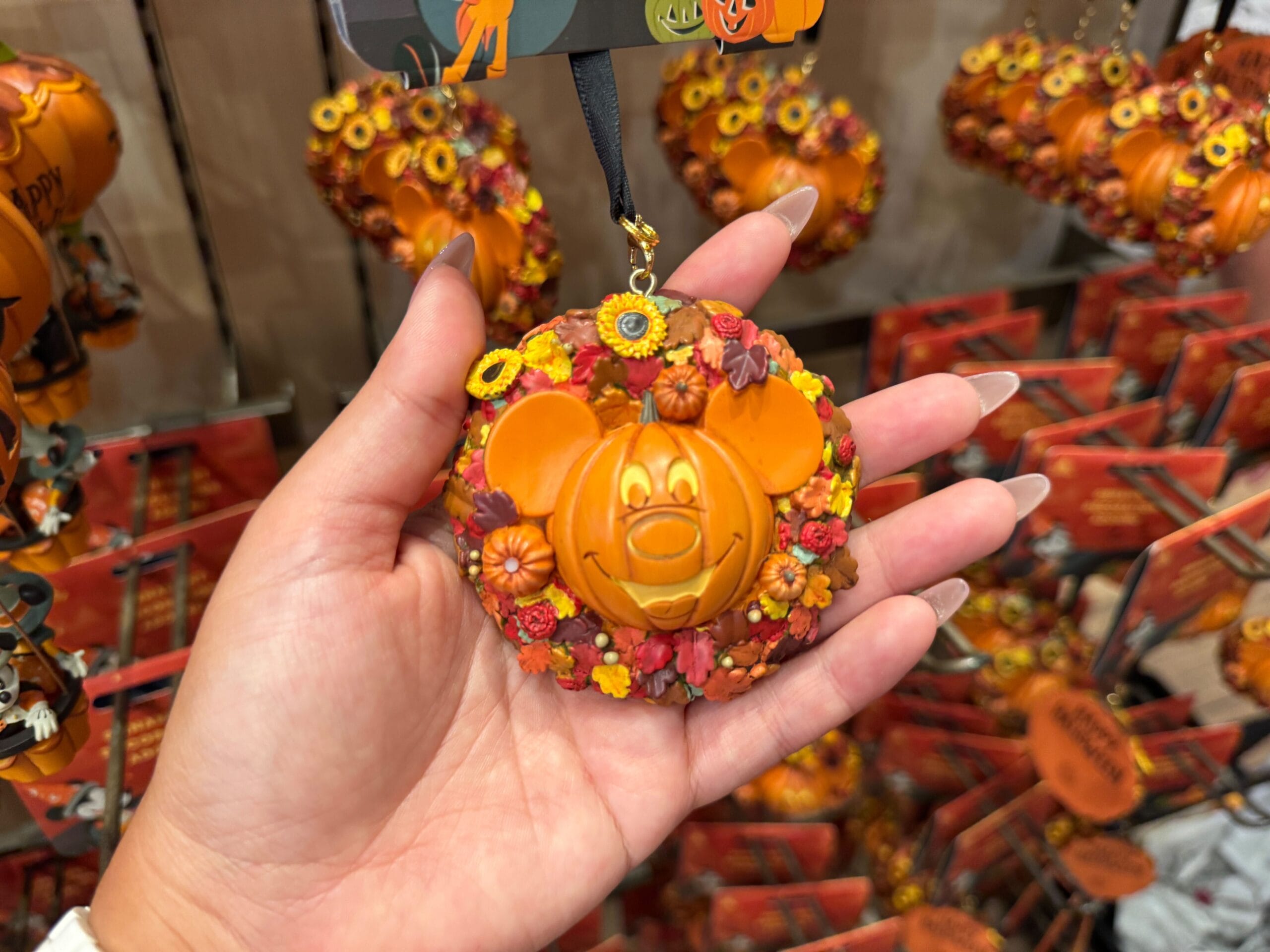 Hand holding a Walt Disney World Halloween wreath ornament with a Mickey Mouse pumpkin face and autumn leaves.