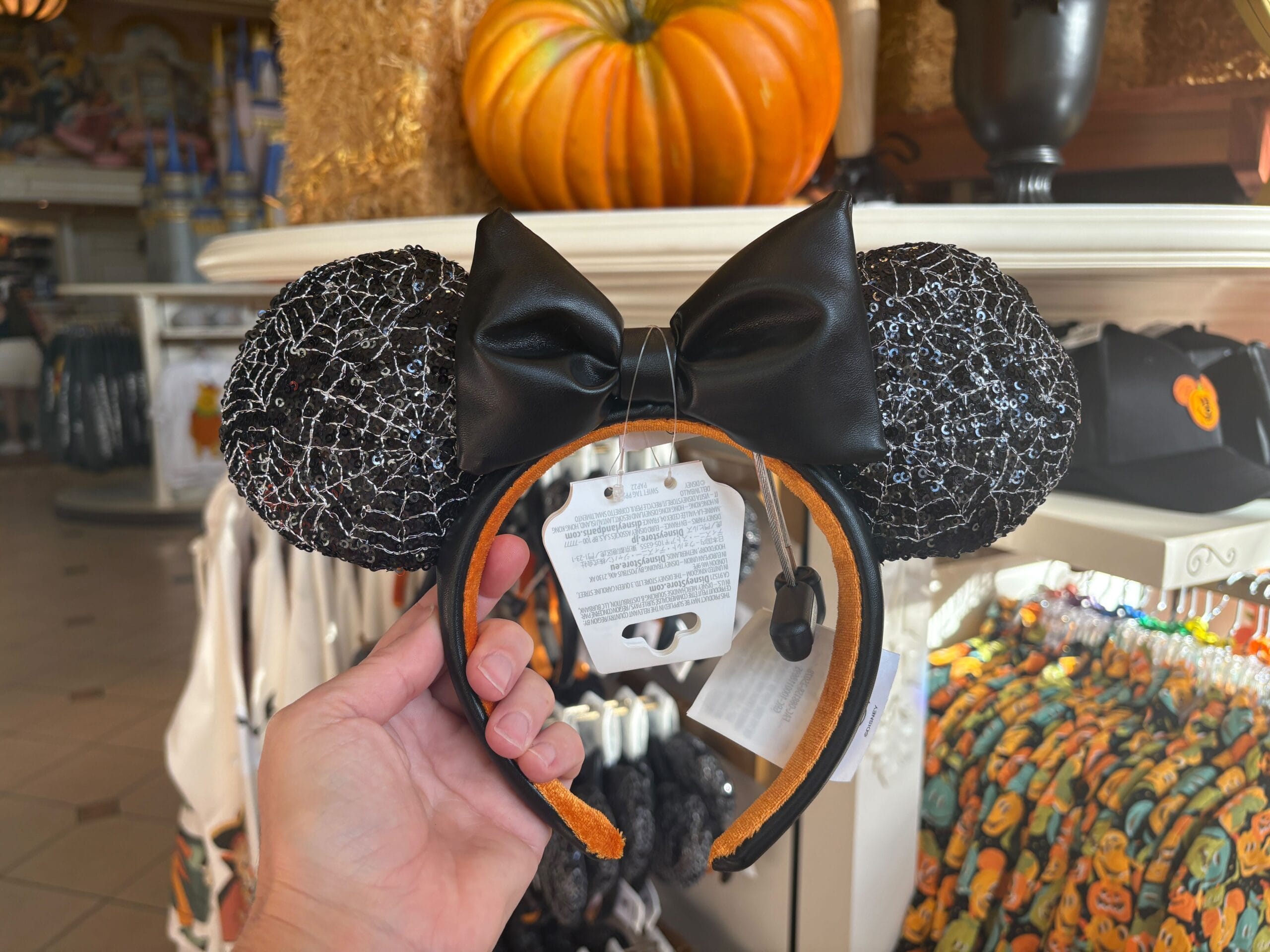 A hand holds black Minnie Mouse ears with a black bow and silver cobwebs—spooky Halloween merchandise at Walt Disney World.