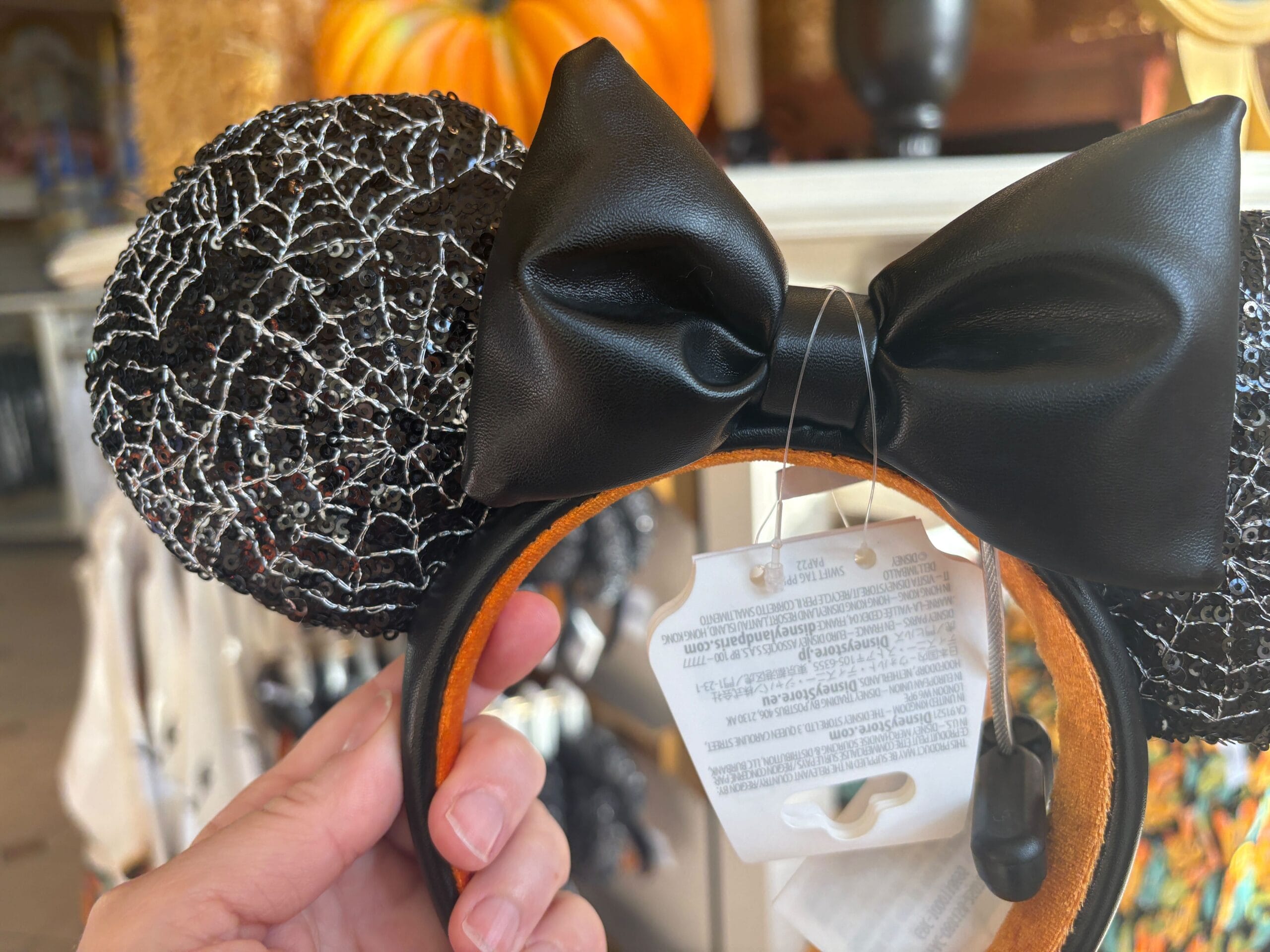 A hand holds black sequined Mickey Mouse ears with a bow, part of Walt Disney World Halloween merchandise.