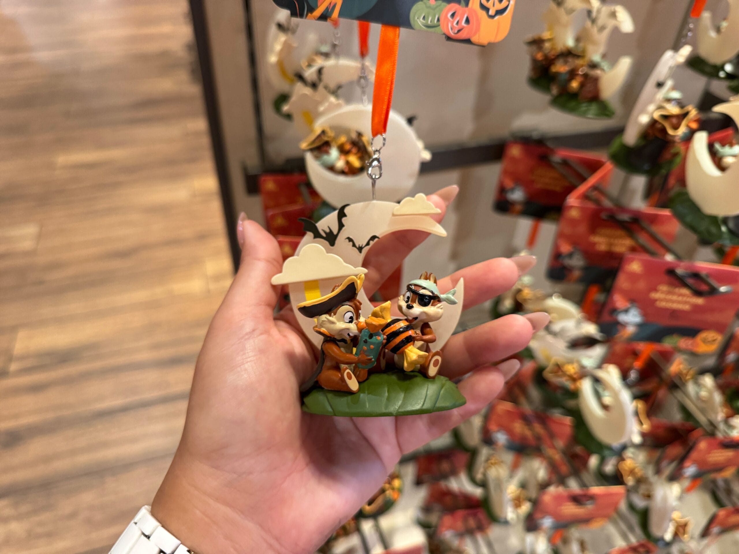 Hand holding a Walt Disney World Halloween Chip and Dale ornament with 2025 merchandise and prices on display shelves.