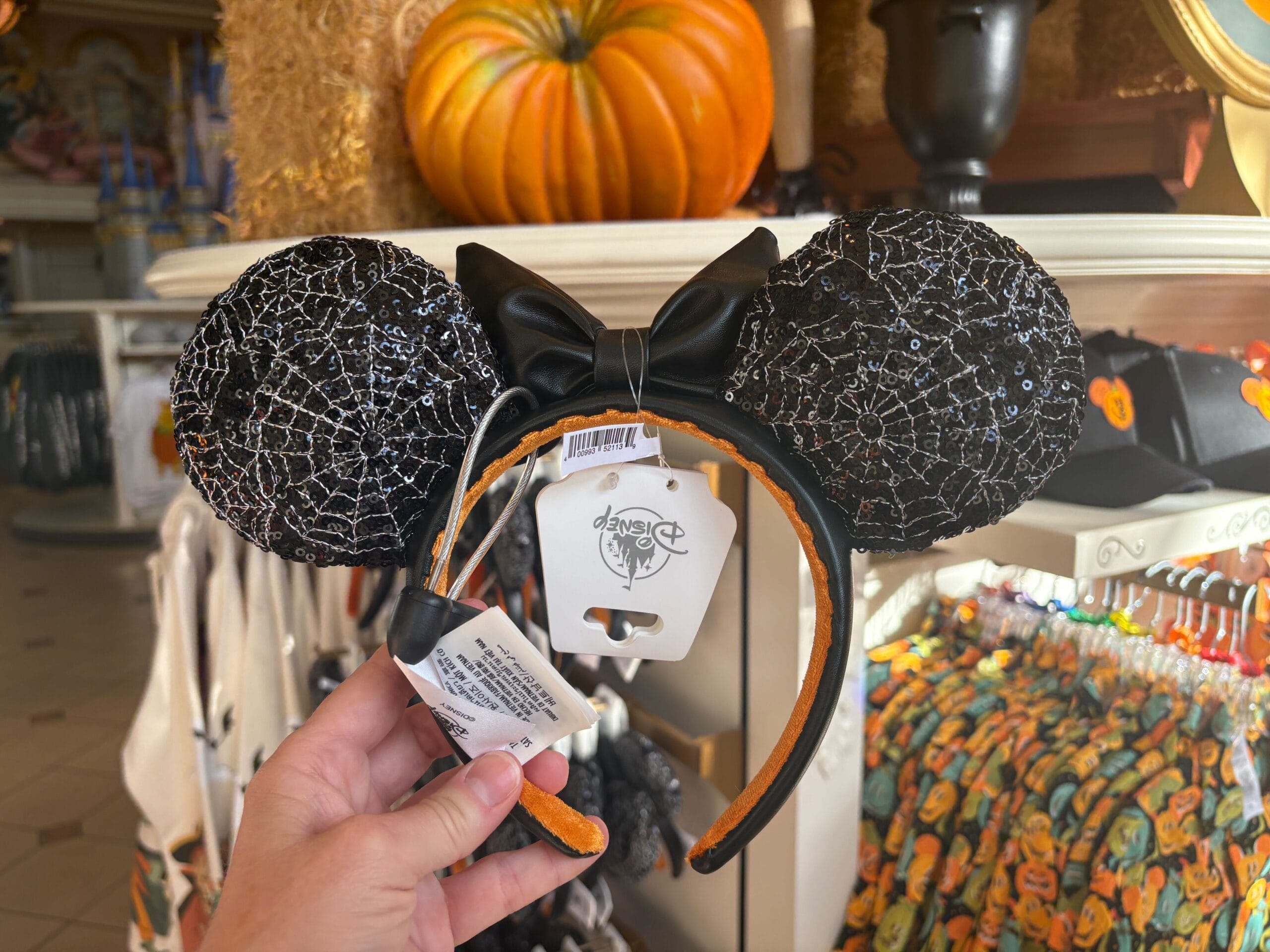 Hand holding black Minnie Mouse ears headband with sparkly spiderweb design, part of Halloween merchandise at Walt Disney World.