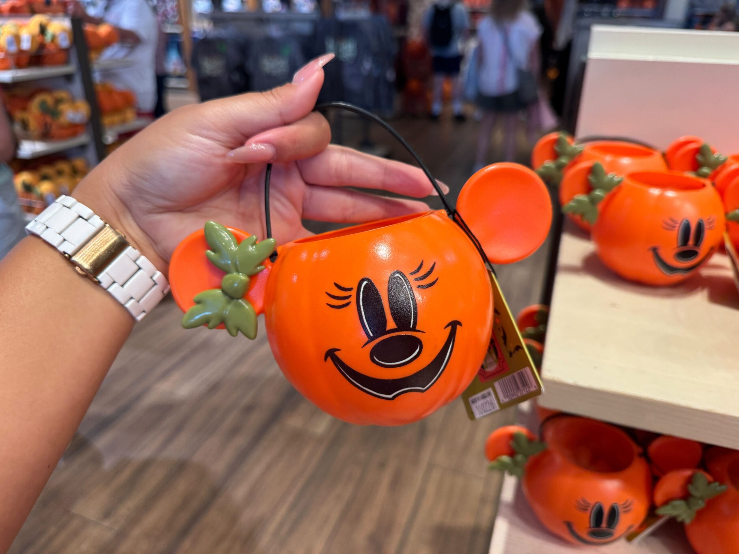 A hand holds a pumpkin-shaped Mickey Mouse bucket among 2025 Halloween merchandise at Walt Disney World.