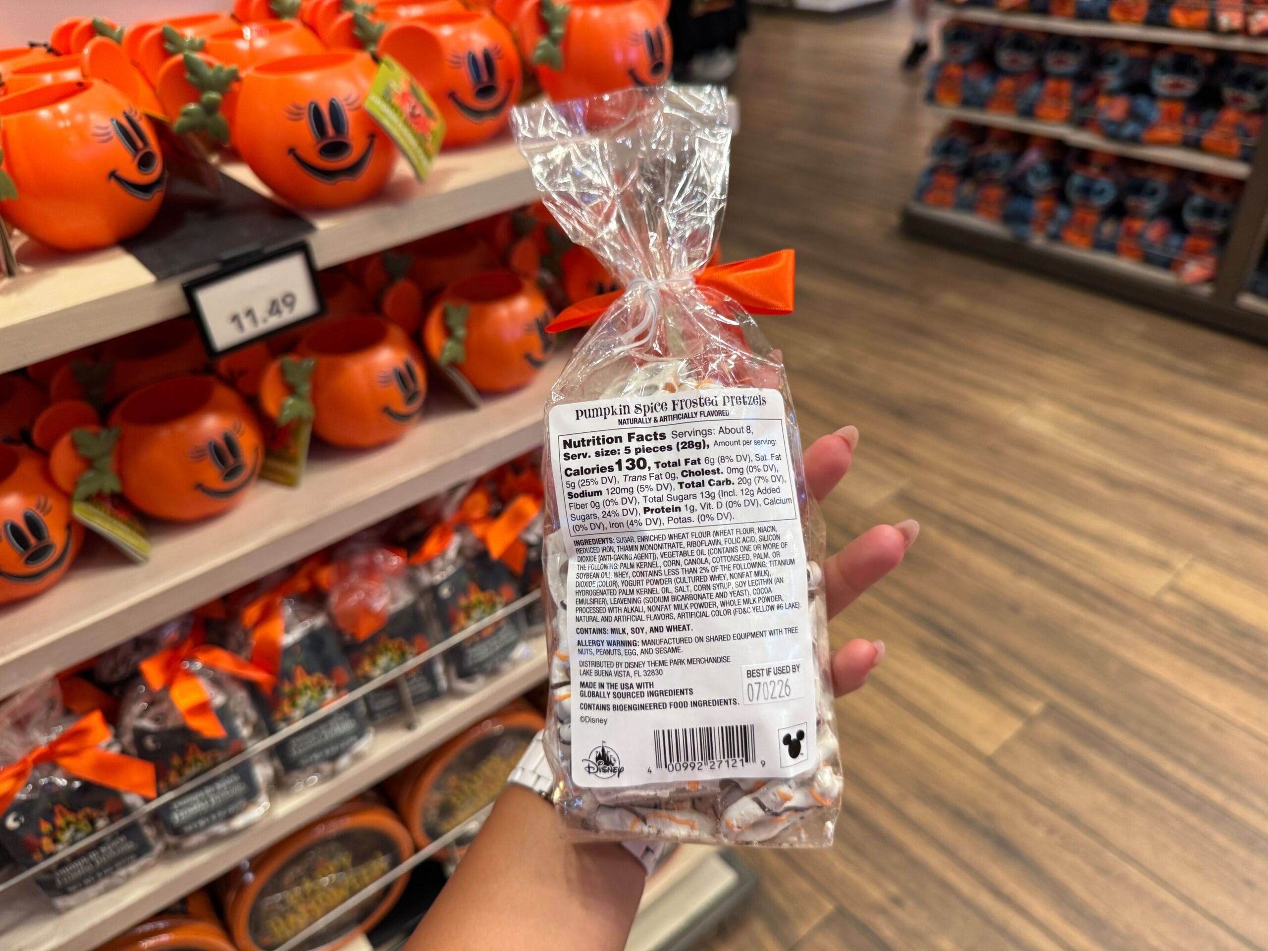 A hand holds pumpkin spice frosted pretzels amid 2025 Halloween merchandise and treats at Walt Disney World.