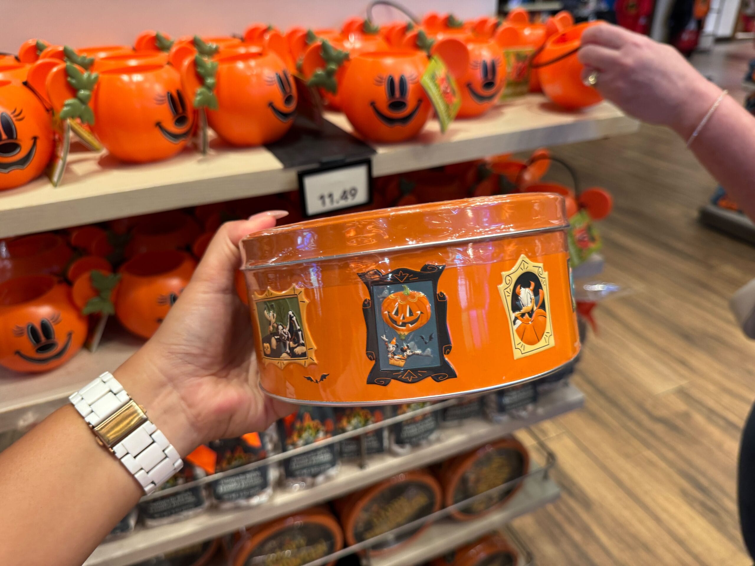 Person holding an orange 2025 Halloween Merchandise tin with Mickey pumpkins in the background at Walt Disney World store.