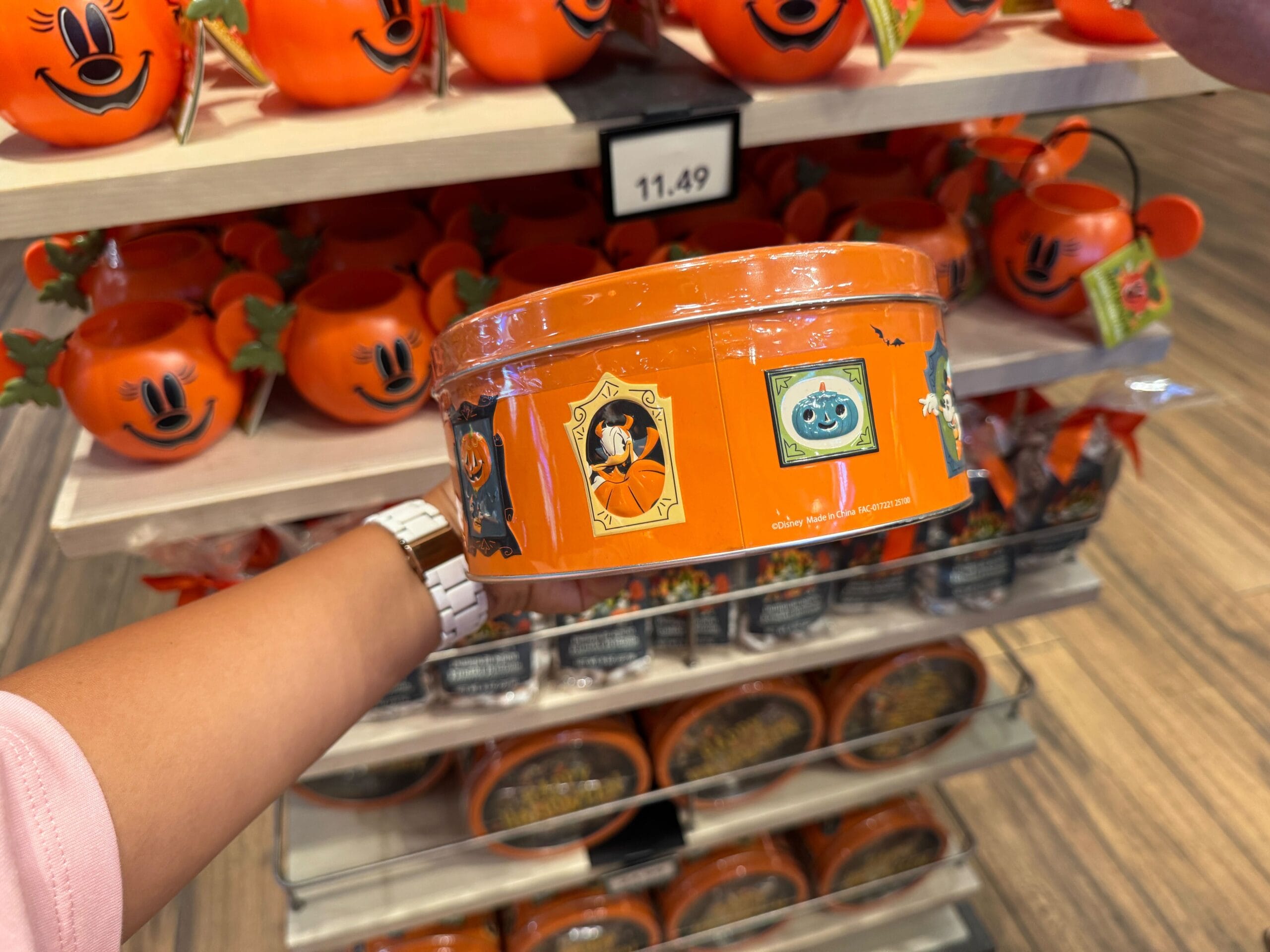 A hand holds an orange Walt Disney World Halloween tin with Mickey and pumpkin designs in a store display.