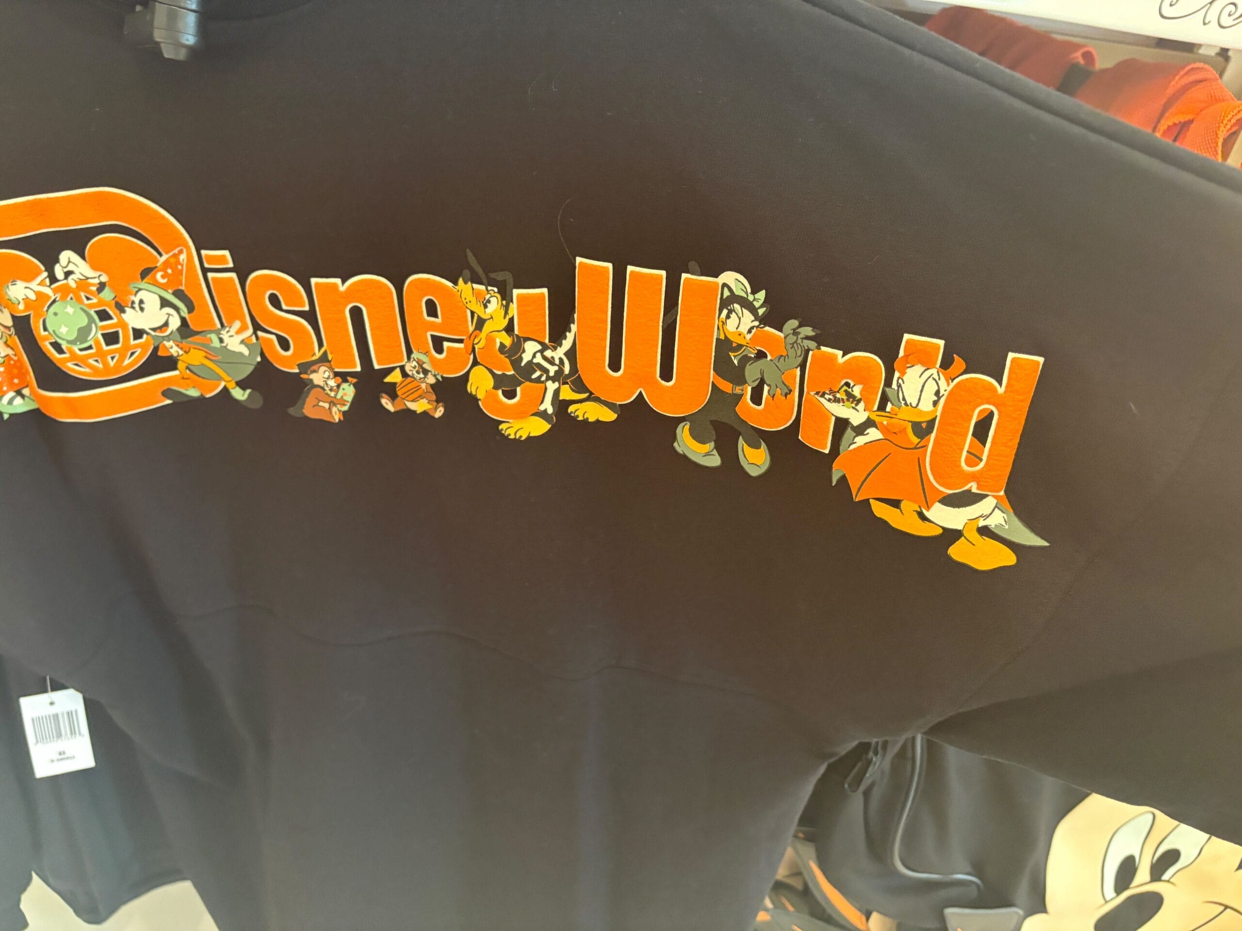 Black Walt Disney World shirt features cartoon characters walking through the orange and yellow “Disney World” logo.