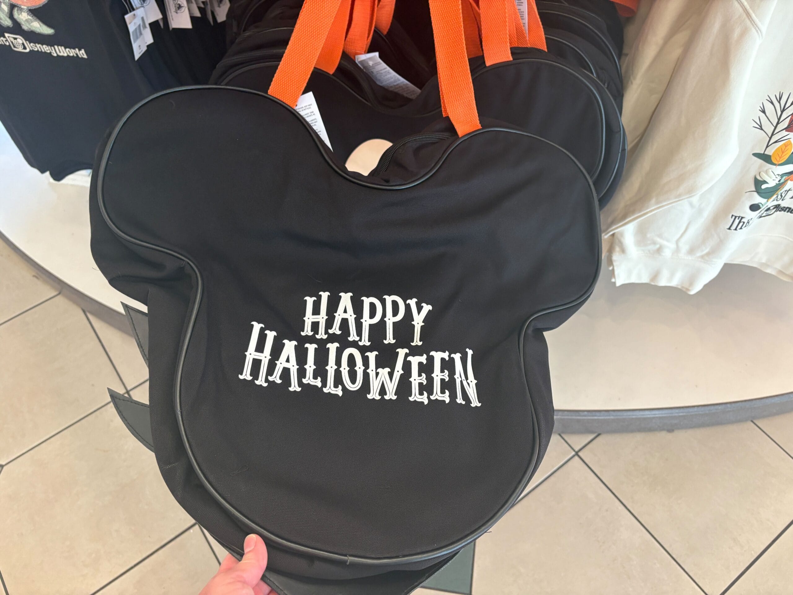 A black Mickey Mouse-shaped Halloween merchandise bag with orange handles and "Happy Halloween" in white text.