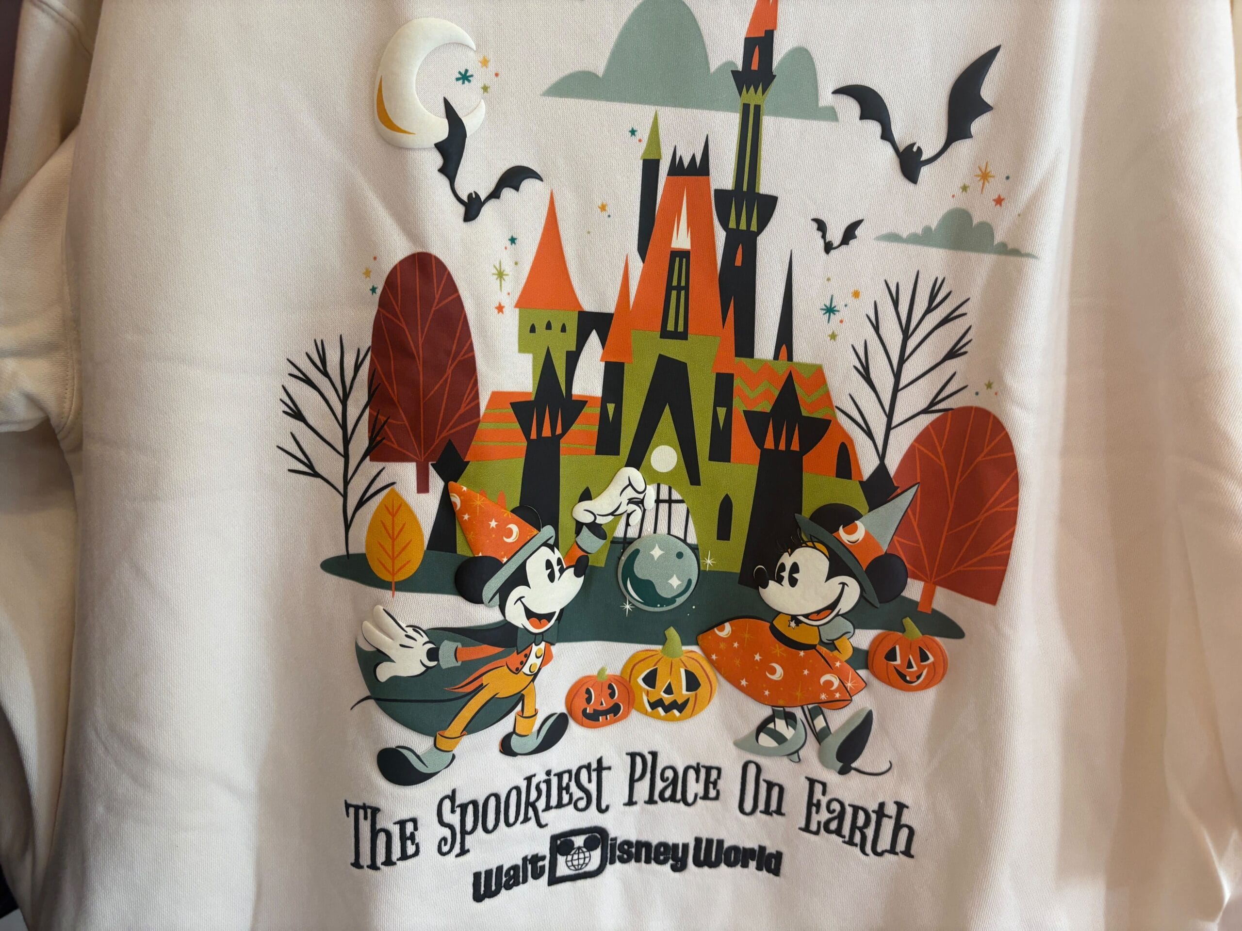 Mickey and Minnie in Halloween costumes at Walt Disney World near a haunted castle with pumpkins and bats.