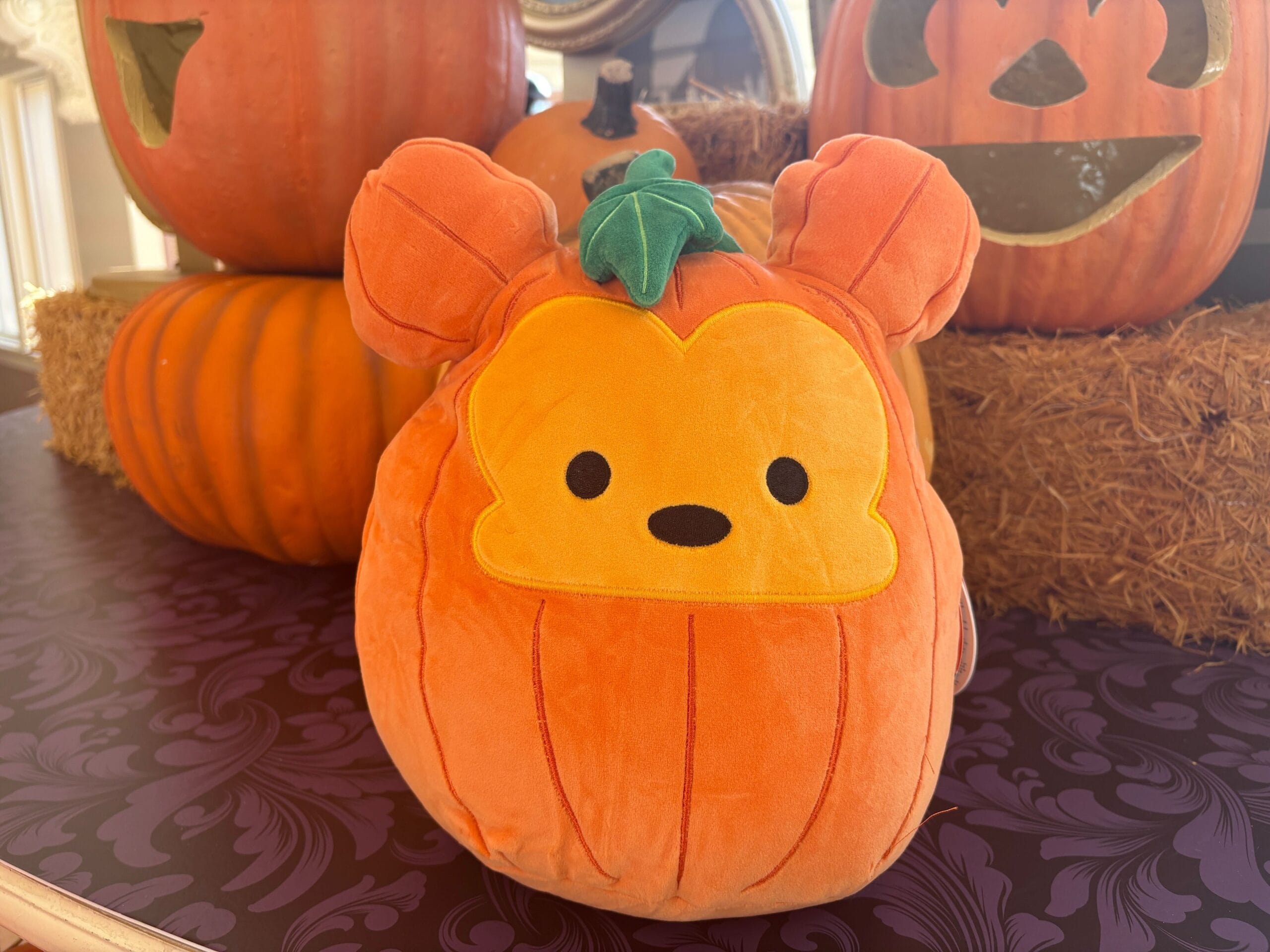 A plush pumpkin with a cute yellow bear face sits on a table, part of Walt Disney World's Halloween merchandise.