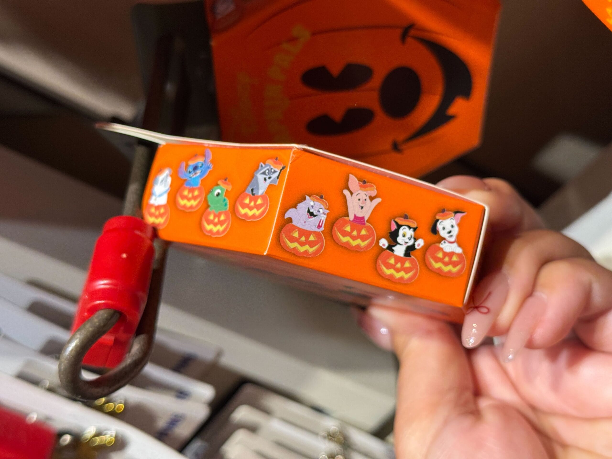 Close-up of a hand holding 2025 Halloween Merchandise with cartoon animals in jack-o'-lanterns on orange packaging.