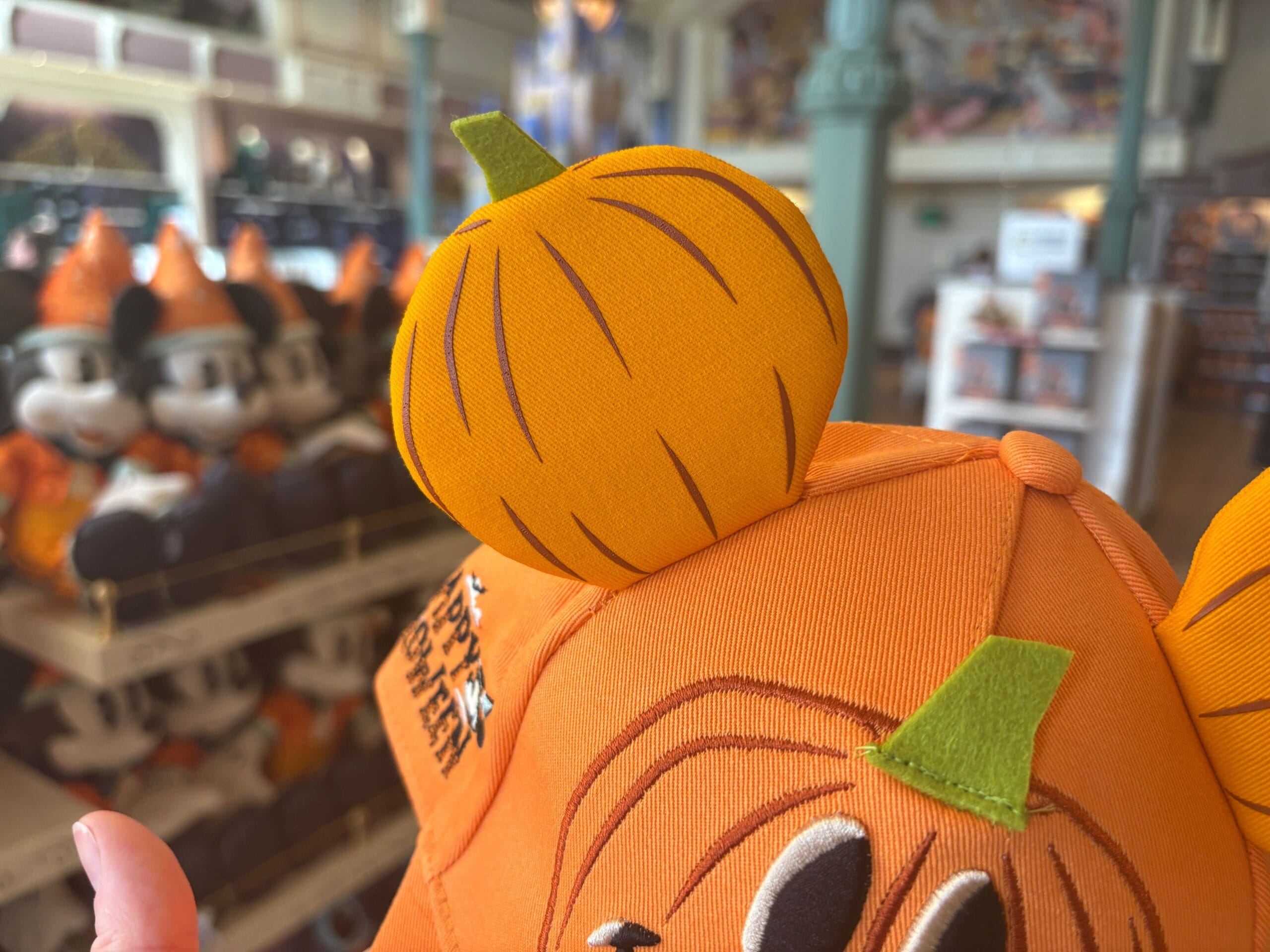 Close-up of a pumpkin-themed Mickey Mouse ear hat among Halloween merchandise at Walt Disney World.