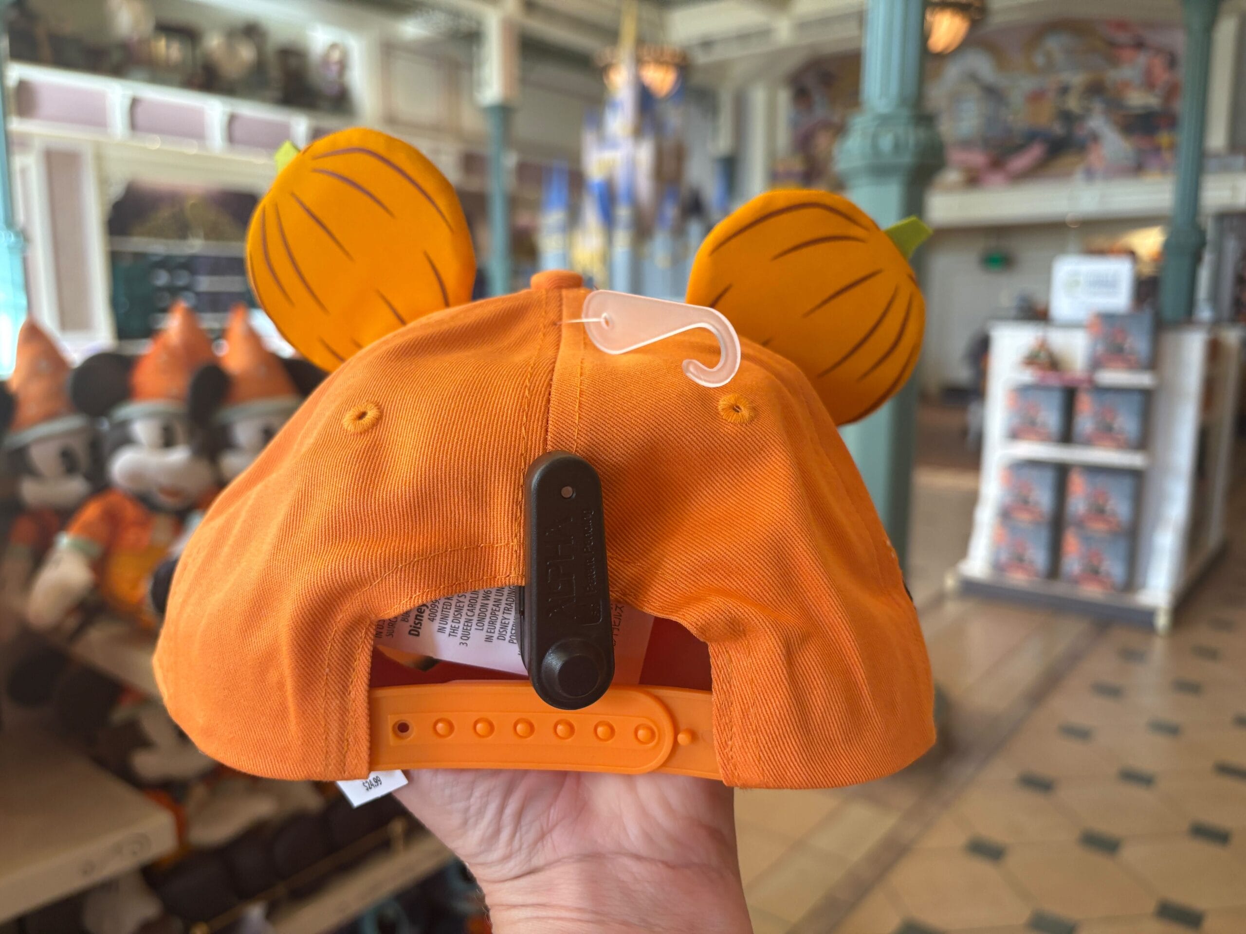 Orange baseball cap with tiger-striped ears, part of Halloween Merchandise at Walt Disney World, held in a store with plush toys.
