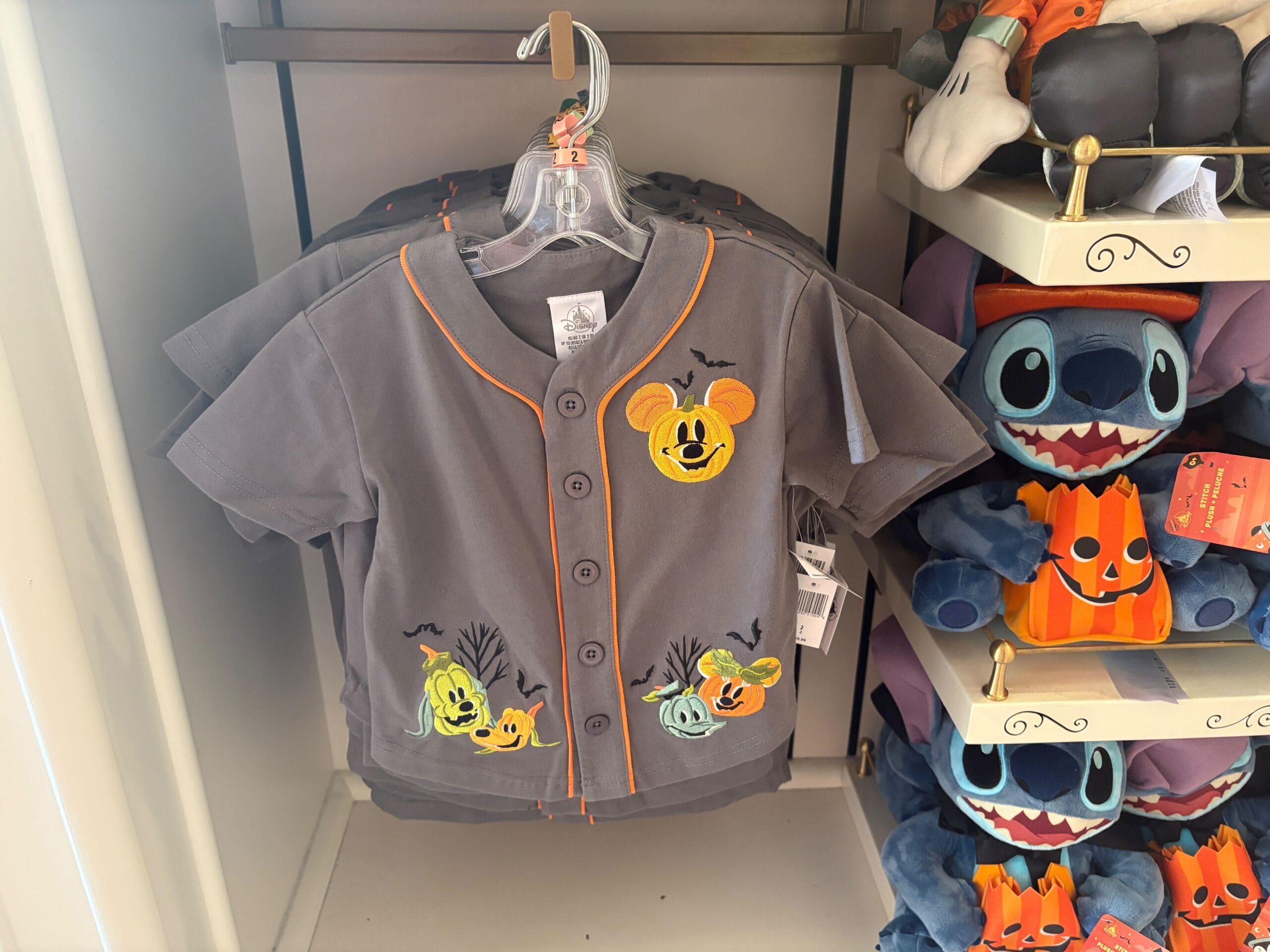 Disney Halloween Merch 2025 - Gray Halloween-themed Mickey Mouse shirt for kids, part of Walt Disney World Halloween merchandise, displayed near Stitch plush toys.