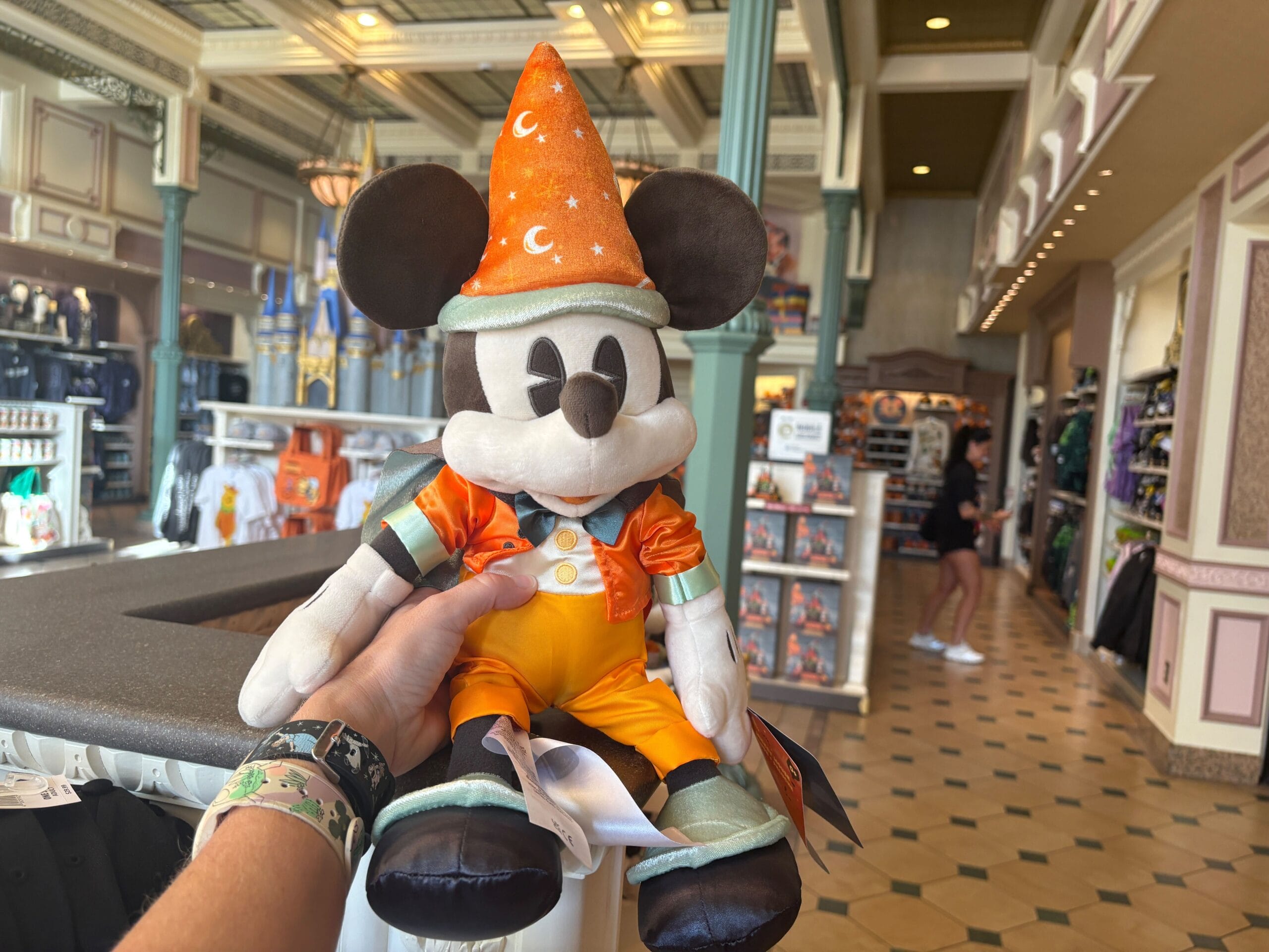 A hand holds a plush Mickey Mouse in an orange wizard costume—Halloween merchandise at Walt Disney World gift shop.