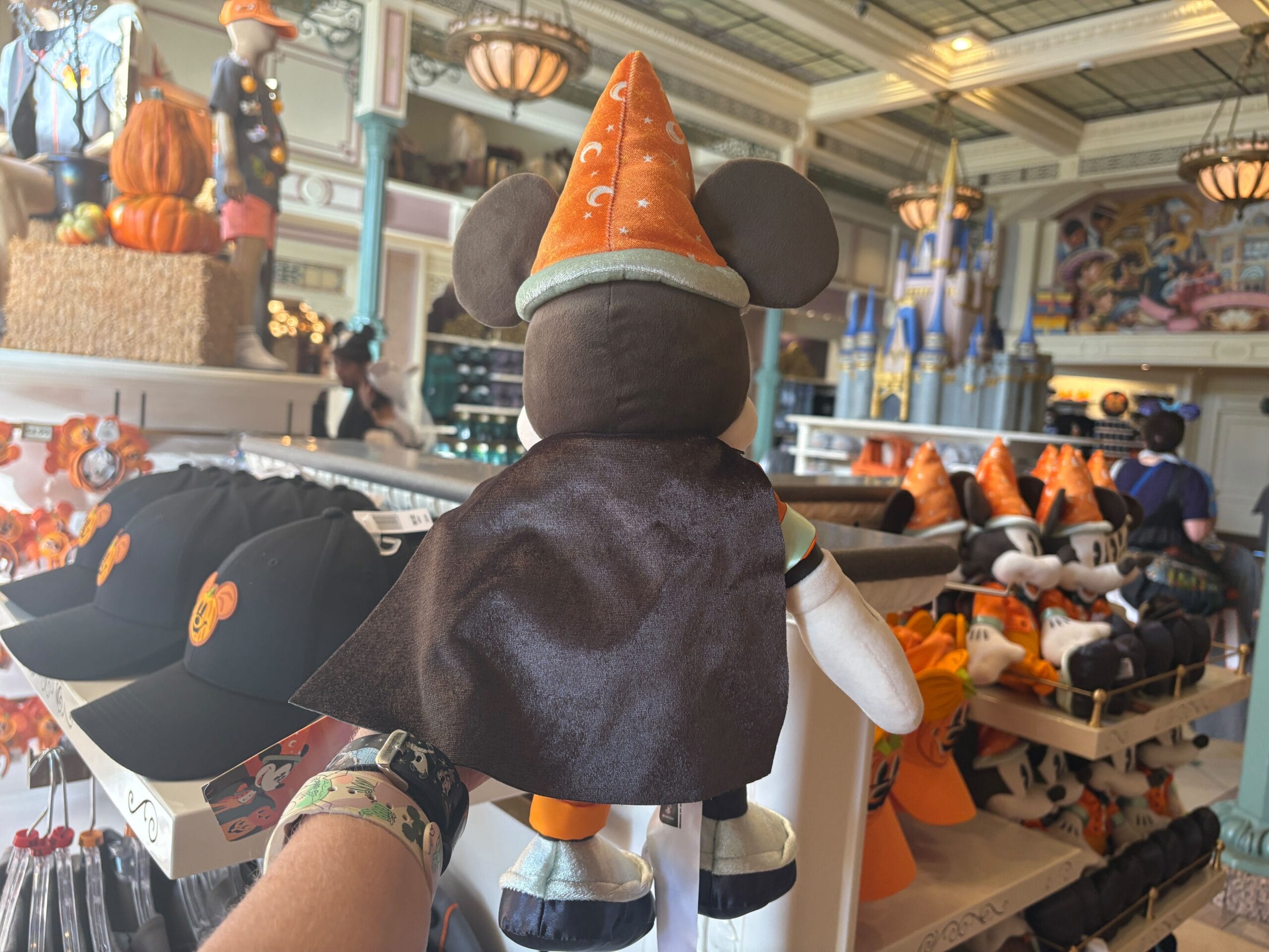 A person holds a Mickey Mouse plush in a wizard hat amid Halloween merchandise at Walt Disney World.