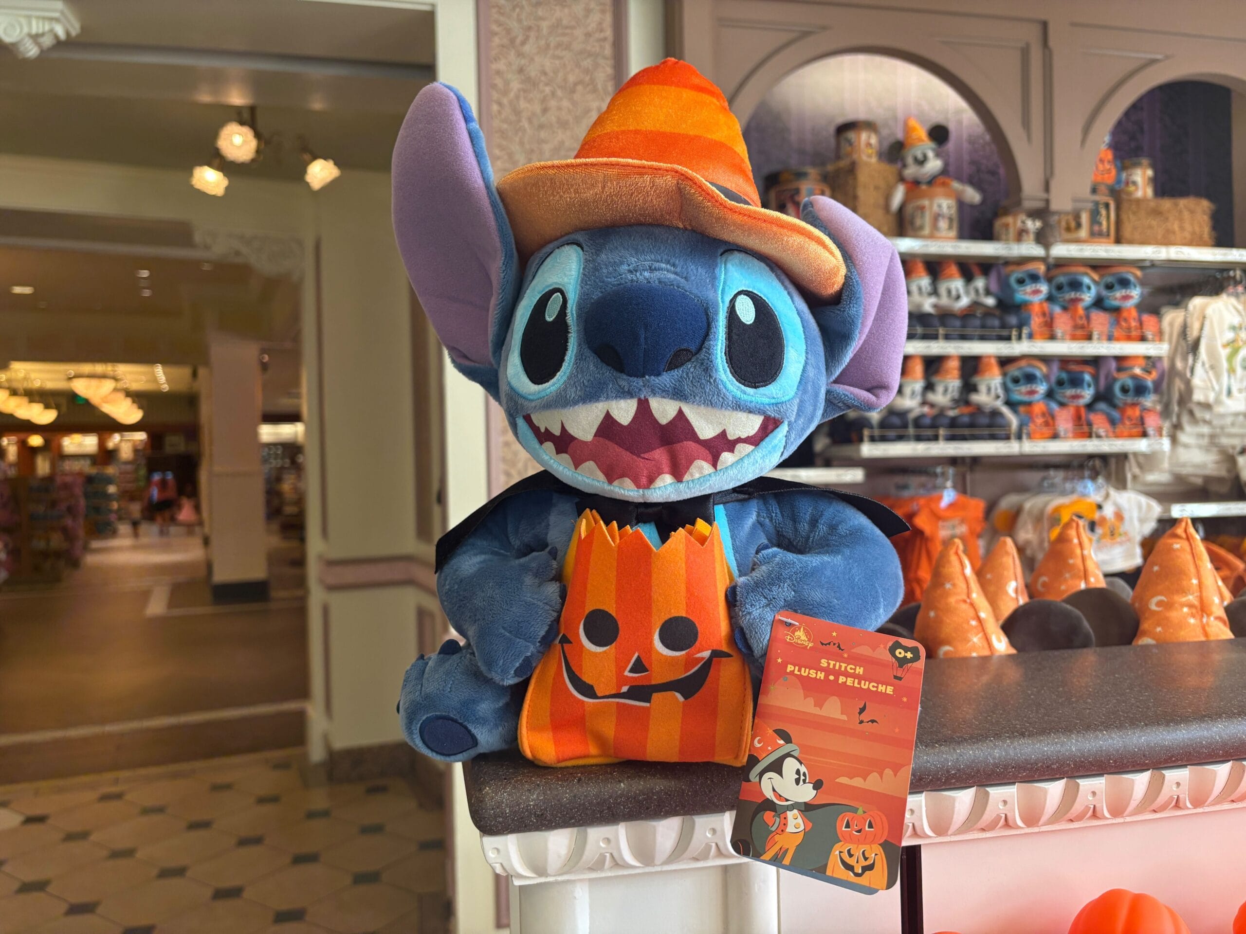 Plush Stitch toy in Halloween merchandise, wearing a hat and cape, holding a pumpkin bag at Walt Disney World store.