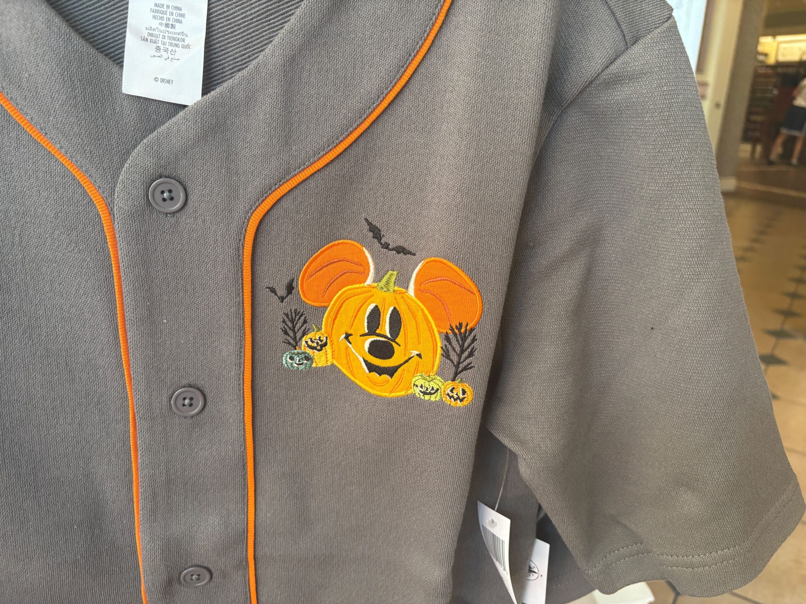 Gray shirt with orange trim, part of Walt Disney World Halloween merchandise, features a Mickey Mouse pumpkin face and festive details.